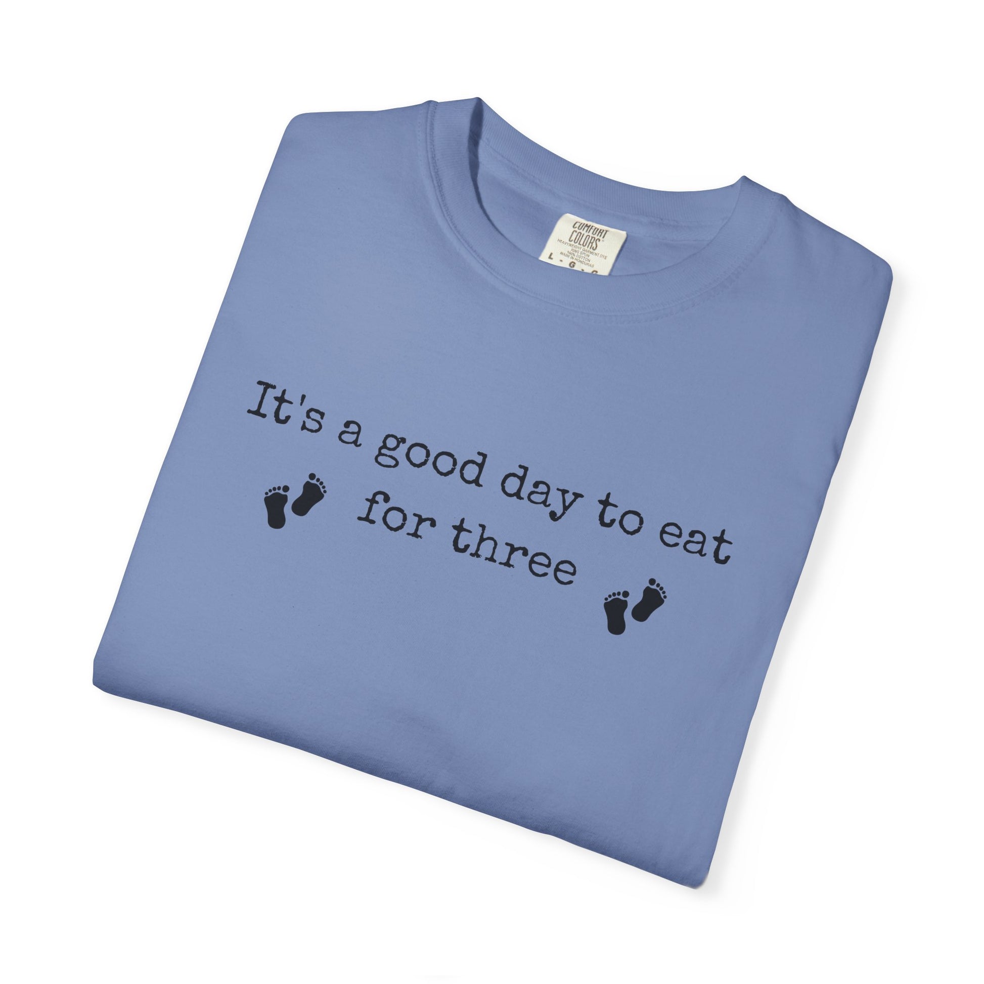 Folded blue t-shirt with text 'It's a good day to eat for three' on a white background