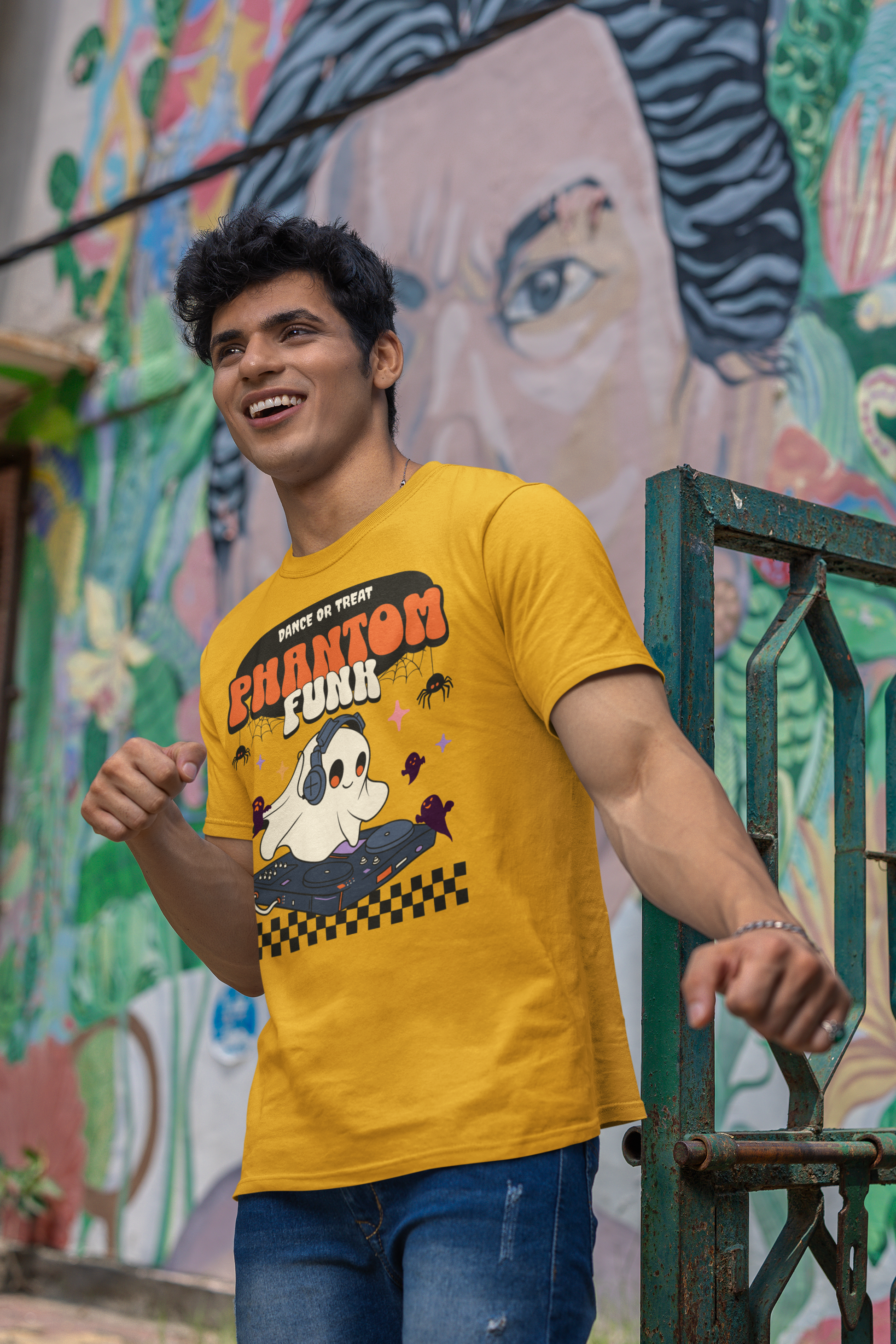 Man wearing a yellow t-shirt with a graphic design in front of a colorful mural.