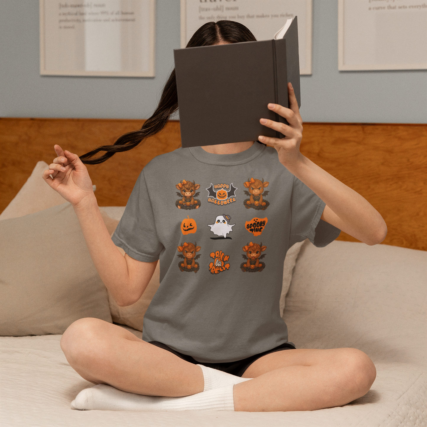 Person wearing a Halloween-themed t-shirt sitting on a couch with a book covering their face.