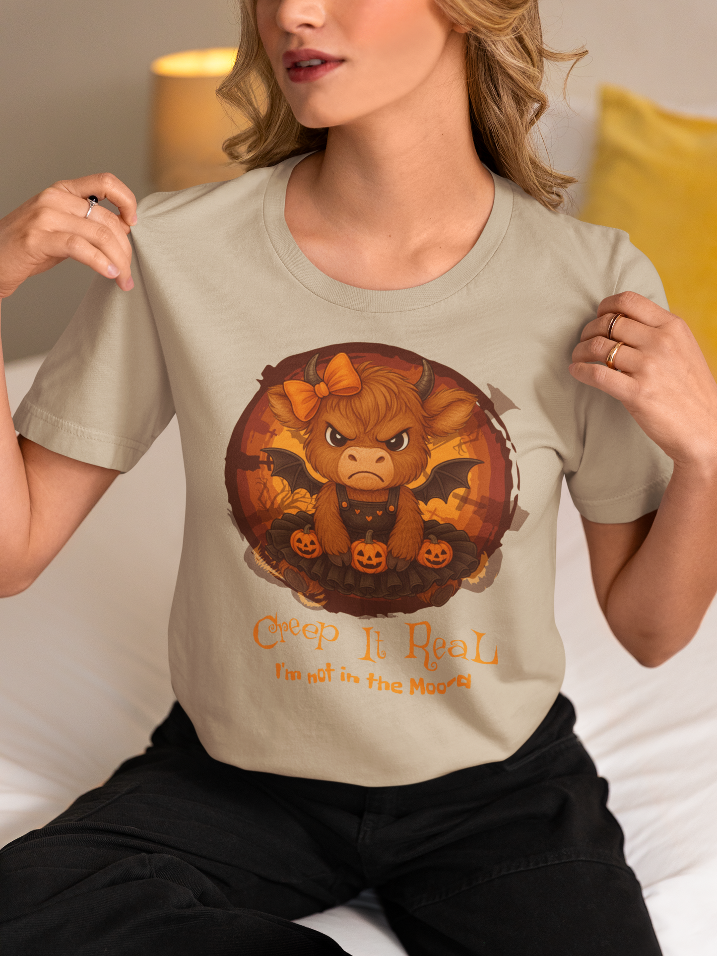 Person wearing a beige t-shirt with a graphic design of a bull and pumpkins, sitting on a couch.