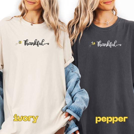 Two people wearing sweatshirts with 'Thankful' text, one in ivory and one in pepper color.