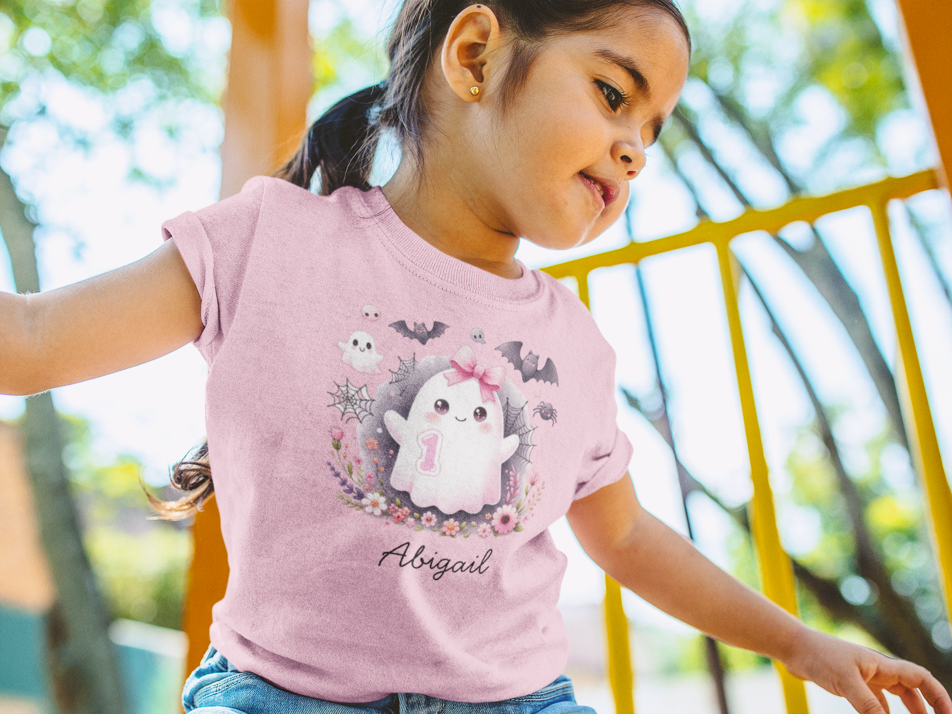 Child wearing a pink t-shirt with a cartoon character and 'Abigail' text, sitting outdoors.