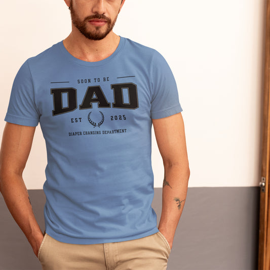 Man wearing a blue t-shirt with 'Soon to be Dad' text on a plain background