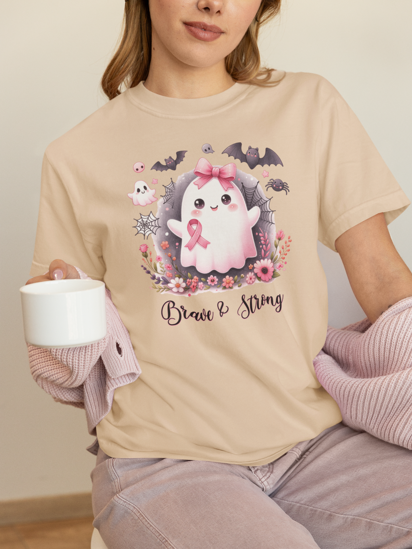 Person wearing a beige t-shirt with a cute ghost design and text, holding a white mug.