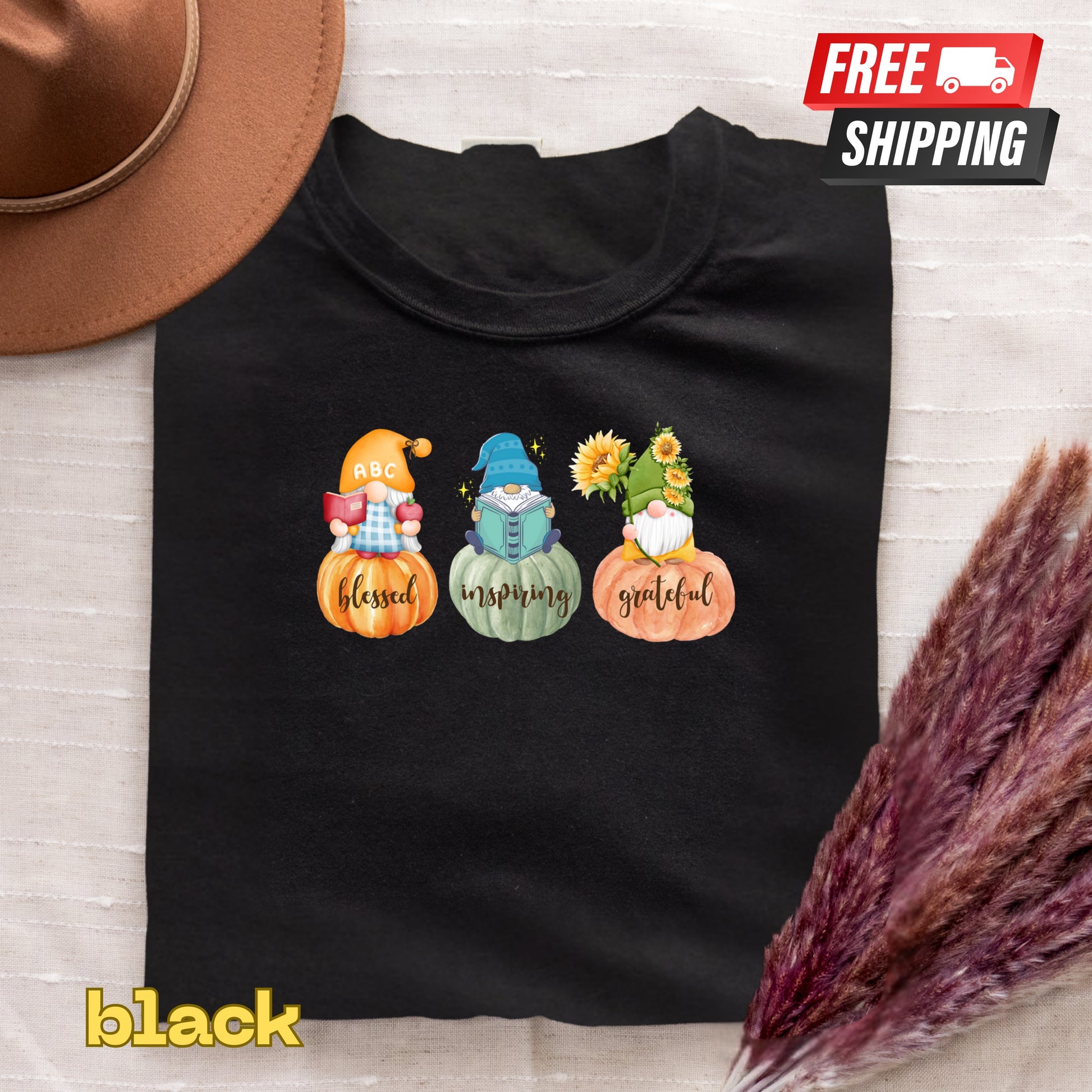 Black t-shirt with gnomes and pumpkins design on a textured surface with a hat and dried plants.