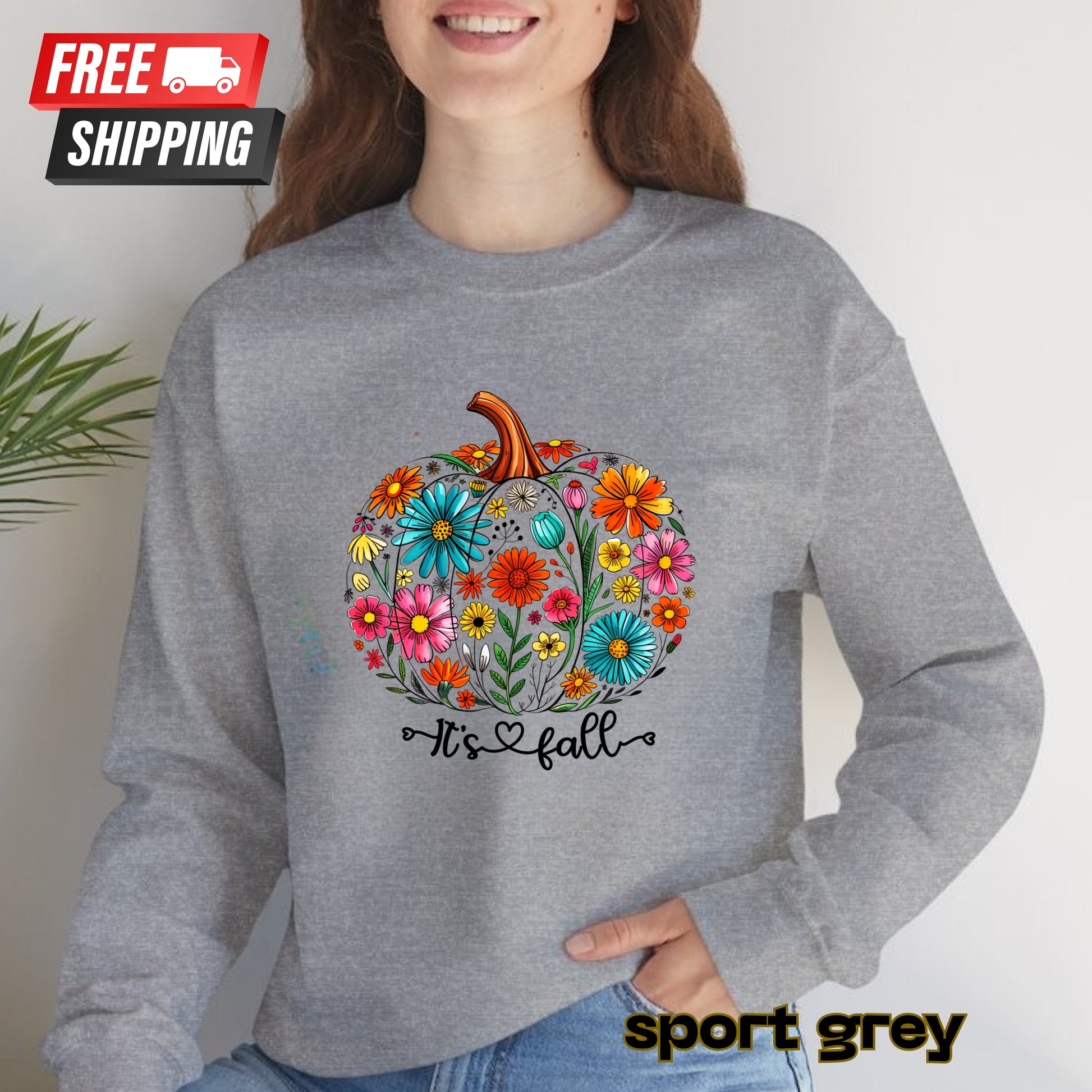 Person wearing a gray sweatshirt with a colorful pumpkin design and 'It's fall' text, on a plain background.