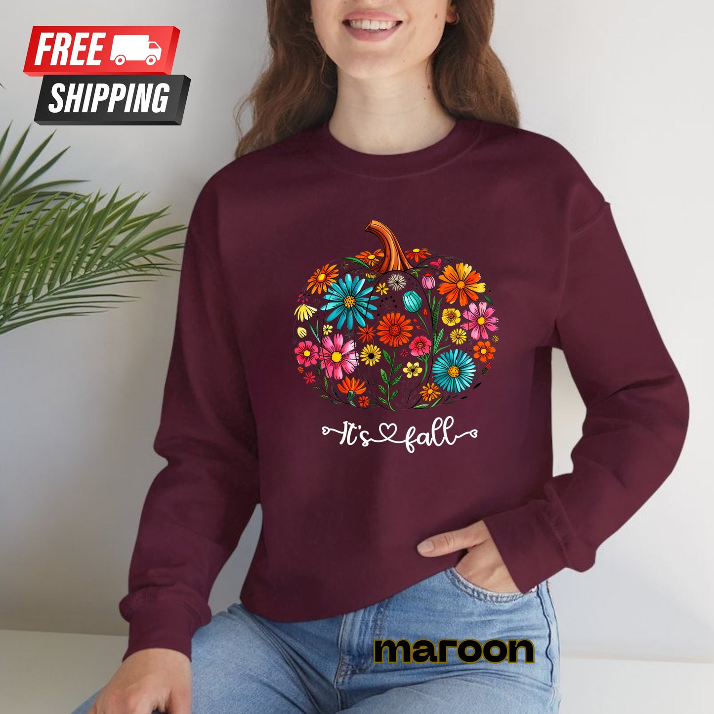 Person wearing a maroon sweatshirt with a colorful pumpkin design and 'It's fall' text, sitting against a white background.