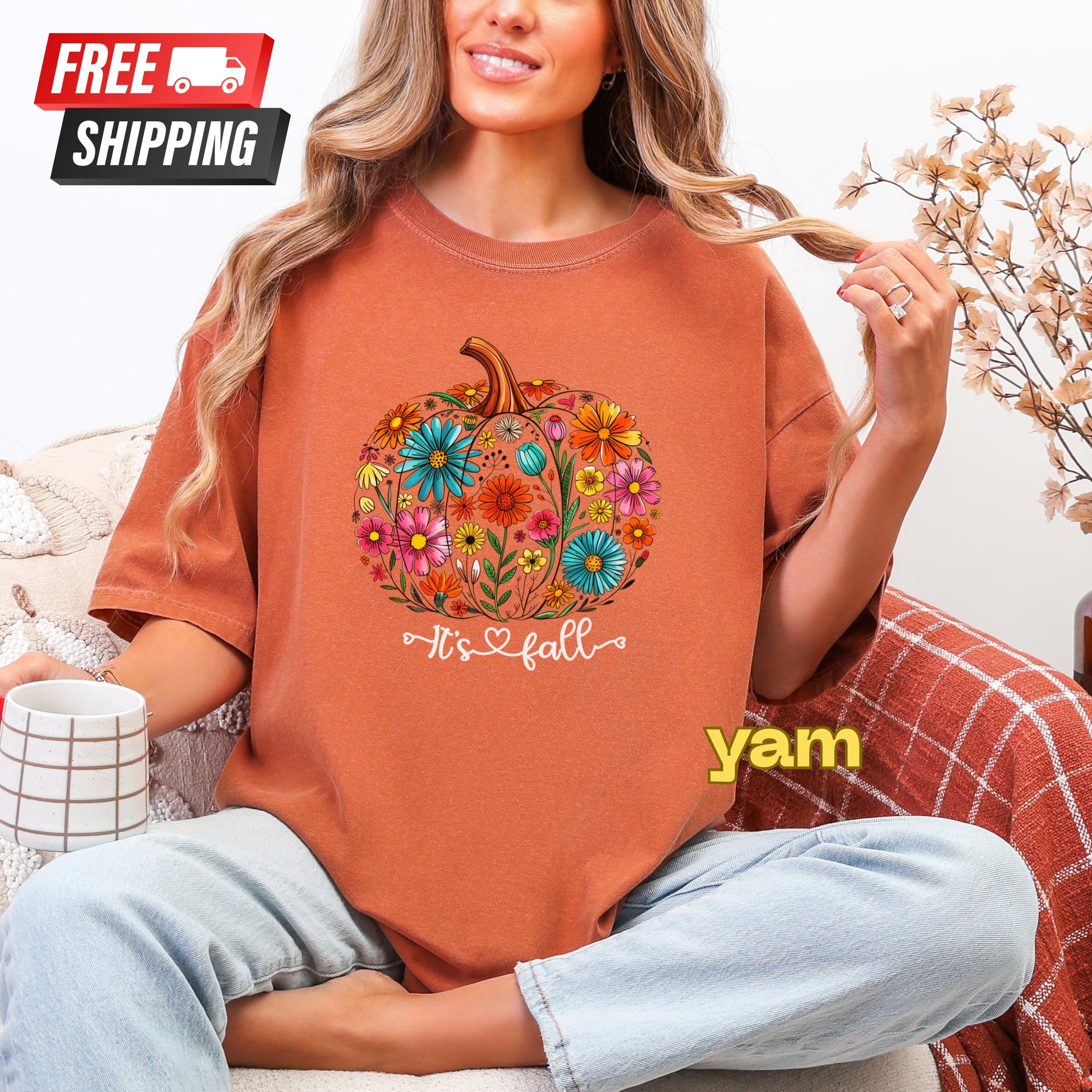 Person wearing a brown t-shirt with a floral pumpkin design and 'It's fall yam' text, sitting on a couch.