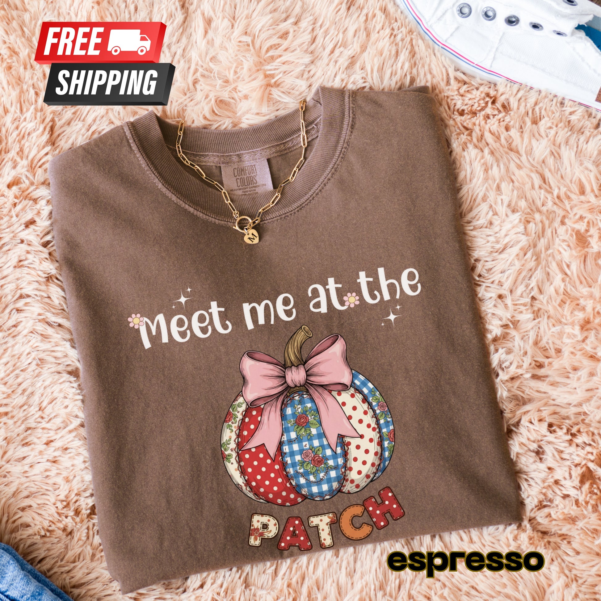 Folded brown sweatshirt with pumpkin design and text 'Meet me at the patch' on a fluffy beige surface.