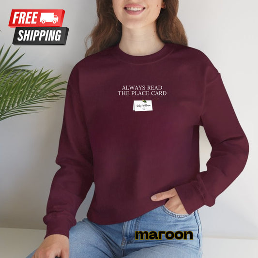 Person wearing a maroon sweatshirt with text and a small card, sitting against a light background.