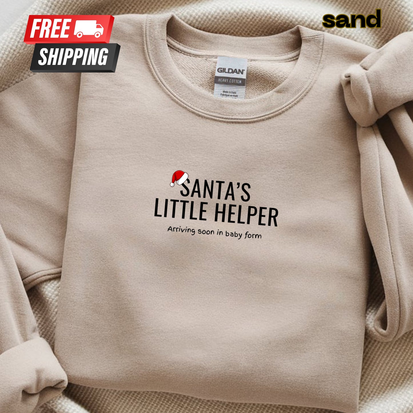 Beige sweatshirt with 'Santa's Little Helper' text and a Santa hat graphic, on a beige background with 'sand' branding.