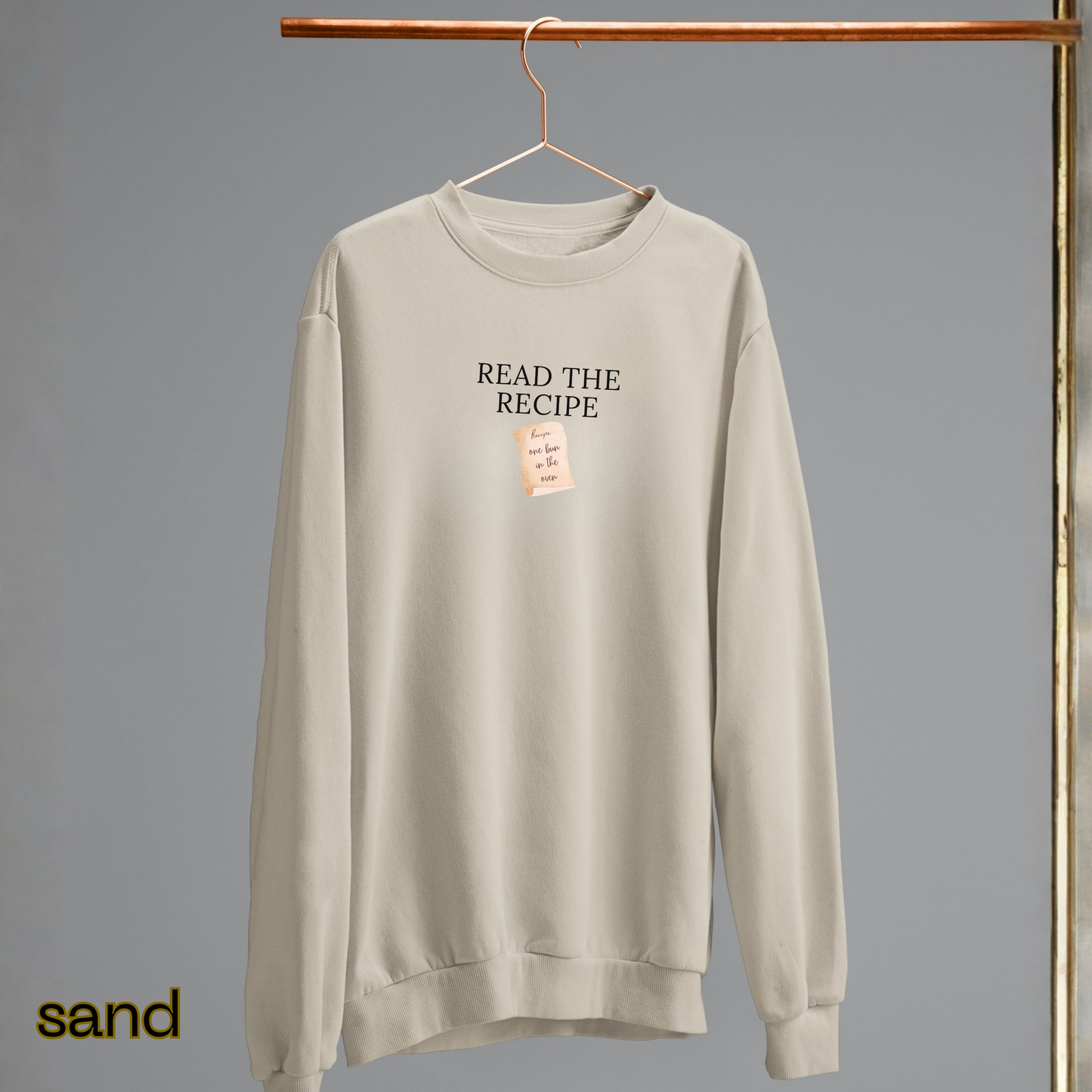 Beige sweatshirt with 'READ THE RECIPE' text on a hanger against a gray background