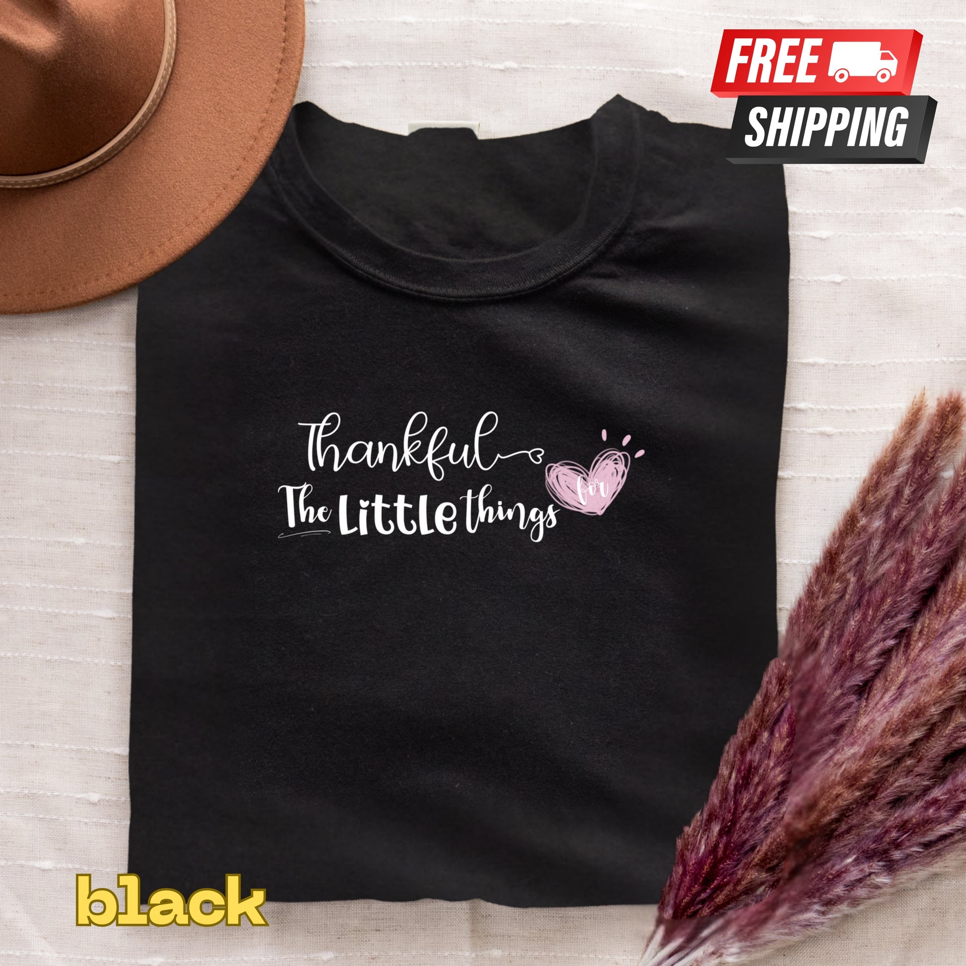 Black t-shirt with 'Thankful for the little things' text and heart design, free shipping label, and 'black' label.