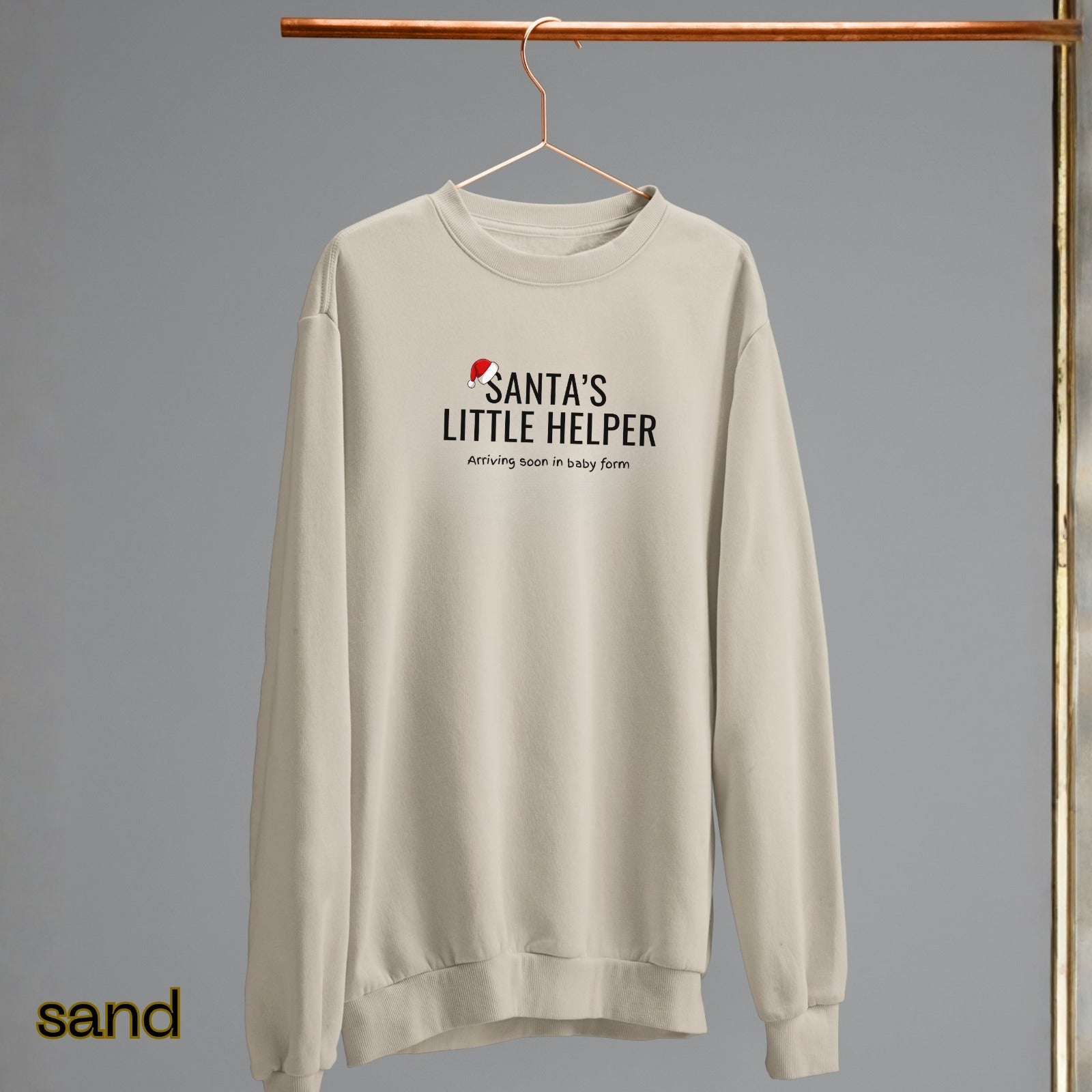 Beige sweatshirt with 'Santa's Little Helper' text on a hanger against a gray background