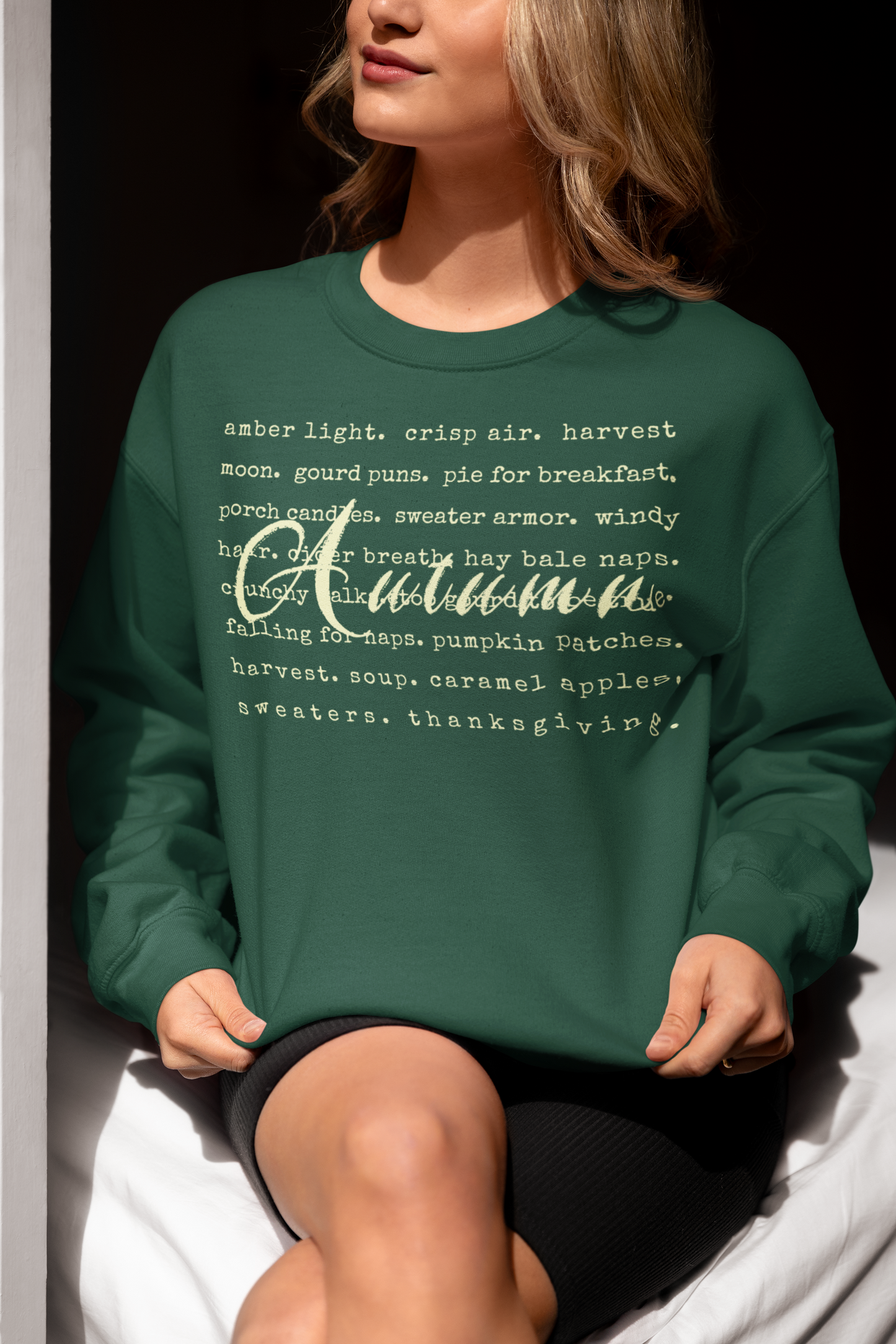 Person wearing a green sweatshirt with 'Autumn' text, sitting on a white surface.