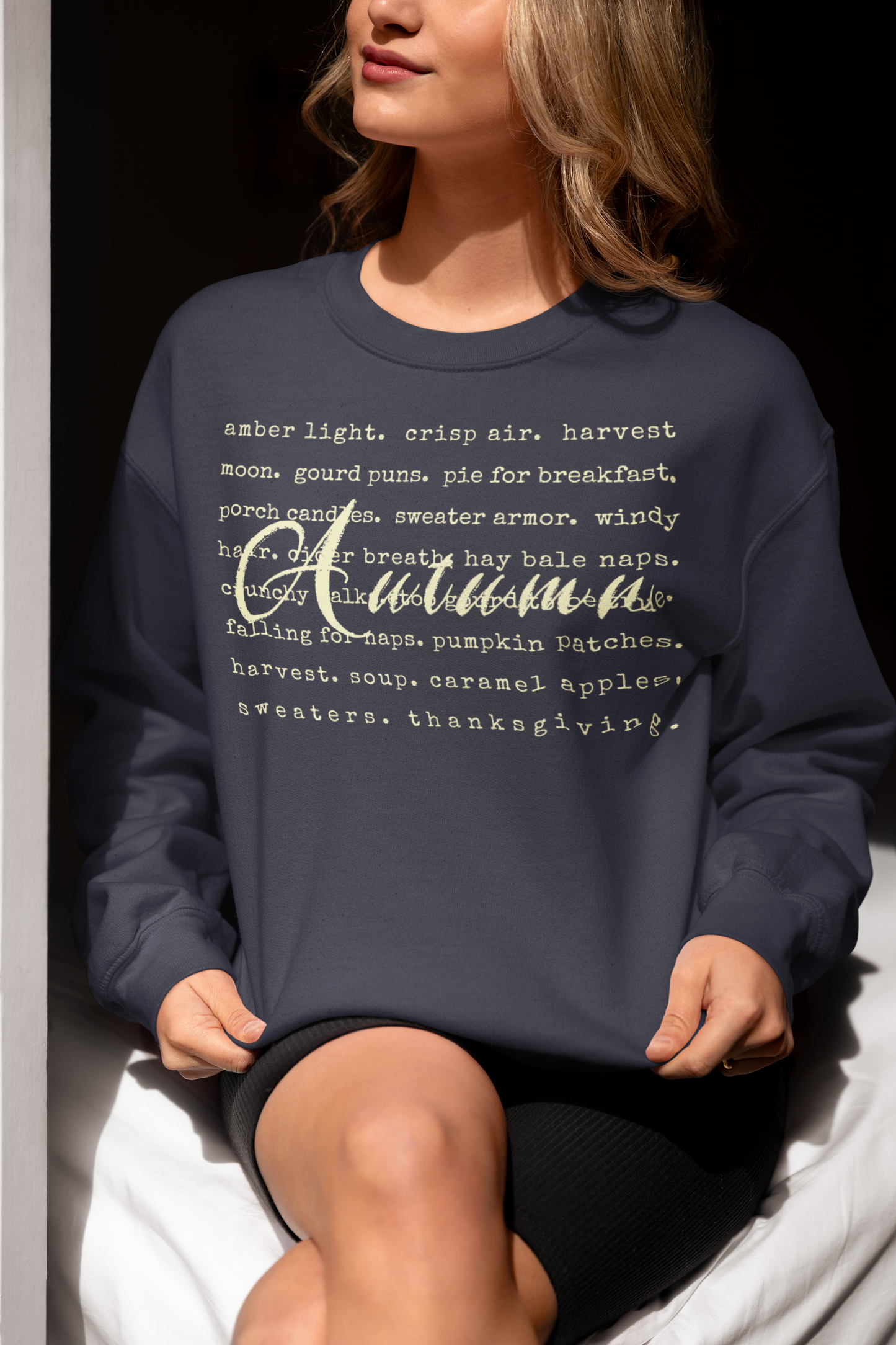 Person wearing a navy blue sweatshirt with 'Autumn' text, sitting on a white surface.