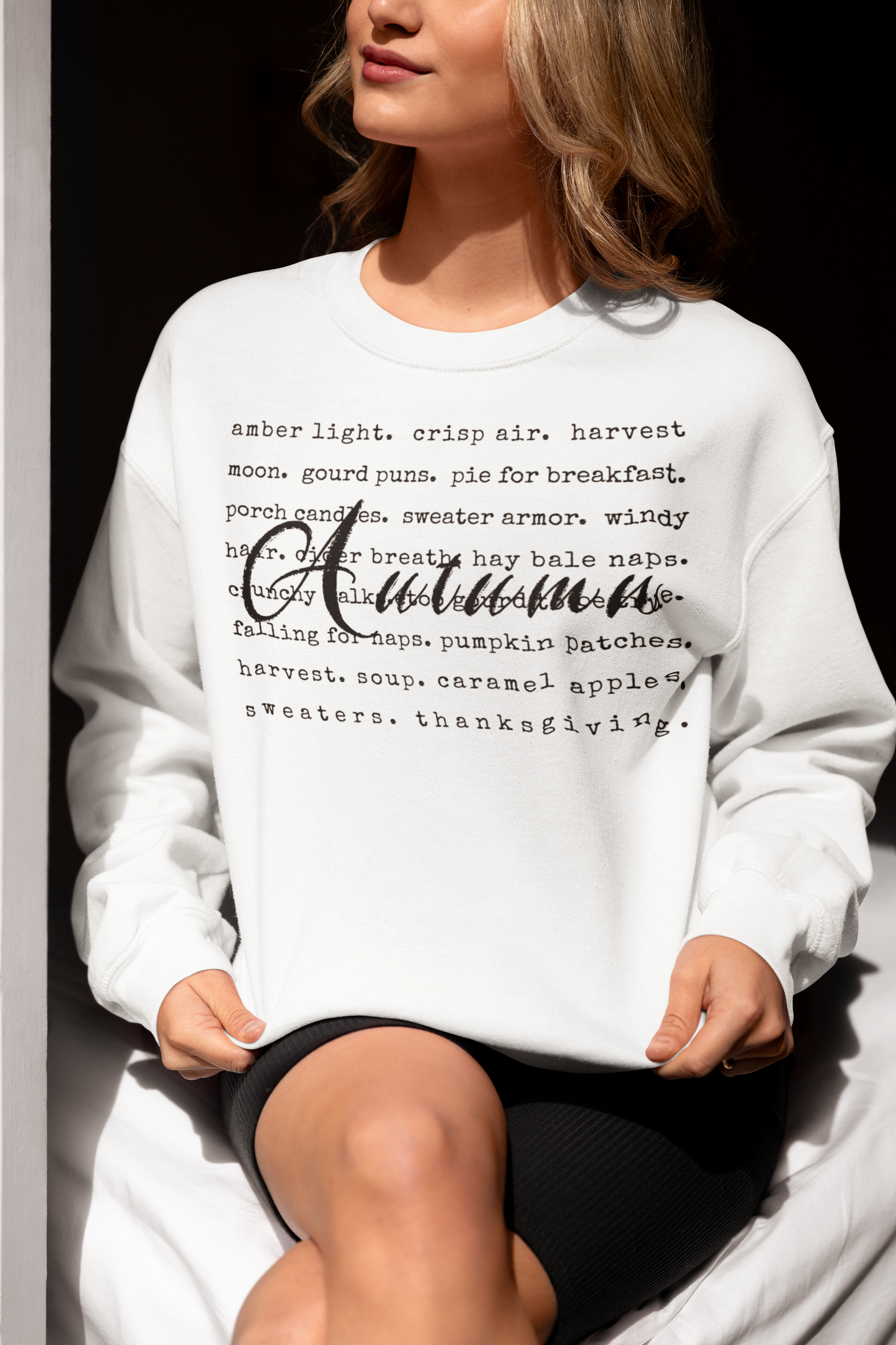 Person wearing a white sweatshirt with autumn-themed text sitting against a dark background