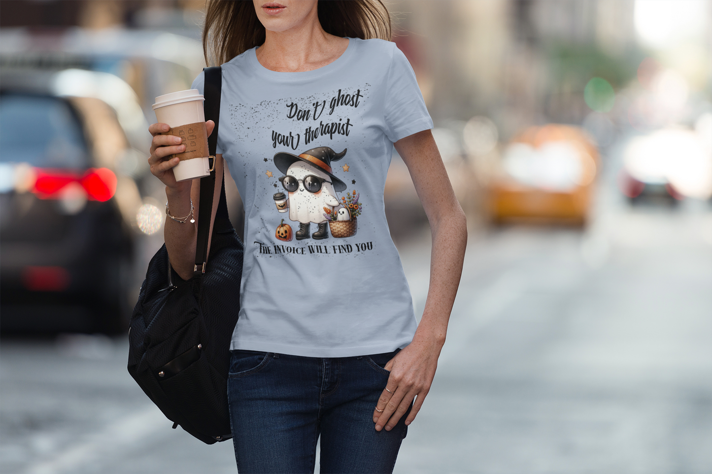 Woman wearing a t-shirt with a graphic and text, holding a coffee cup on a city street.