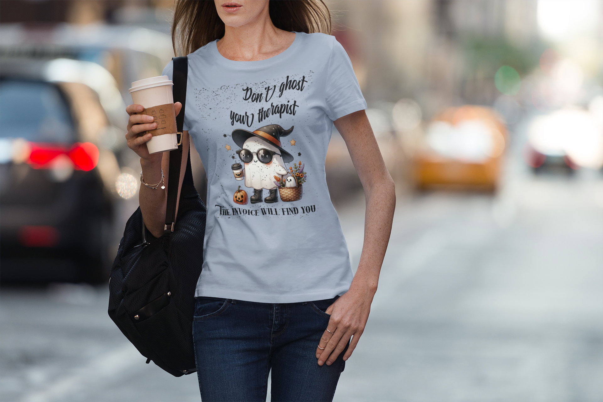 Woman wearing a t-shirt with a graphic and text, holding a coffee cup on a city street.