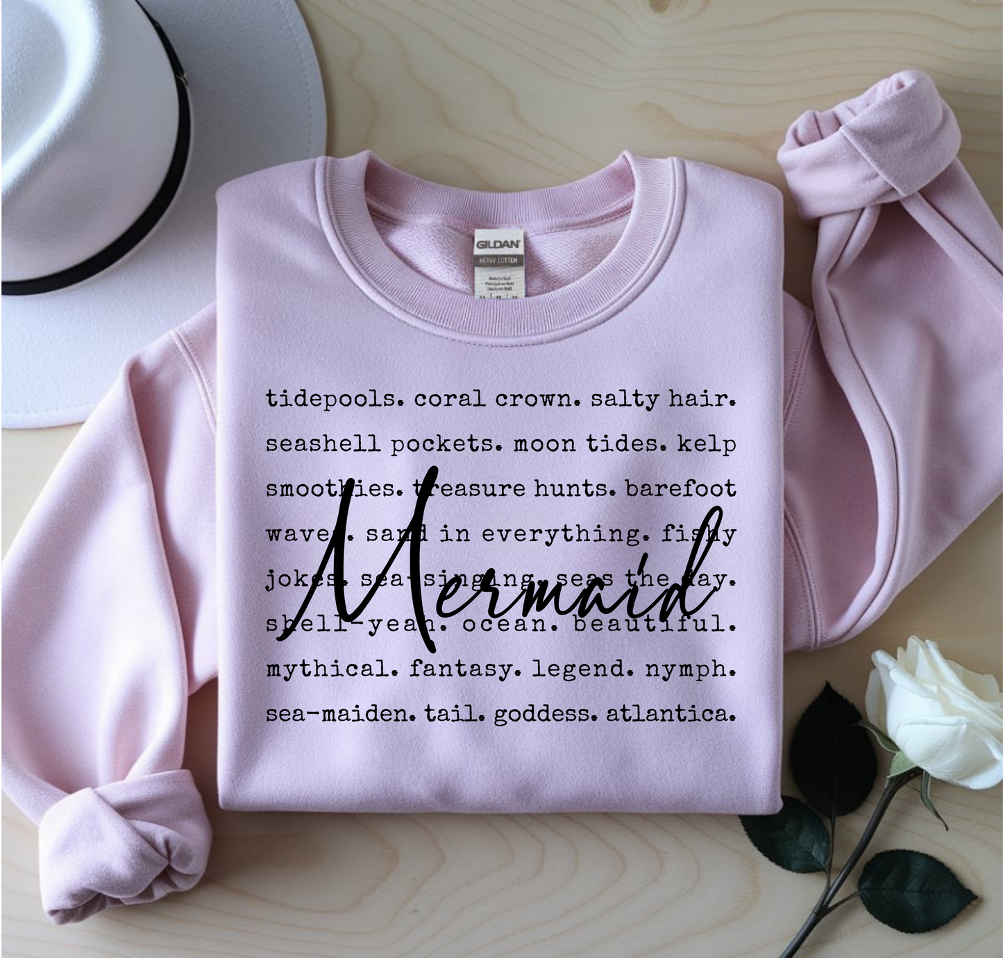 Pink sweatshirt with text design on a wooden surface with a white rose.