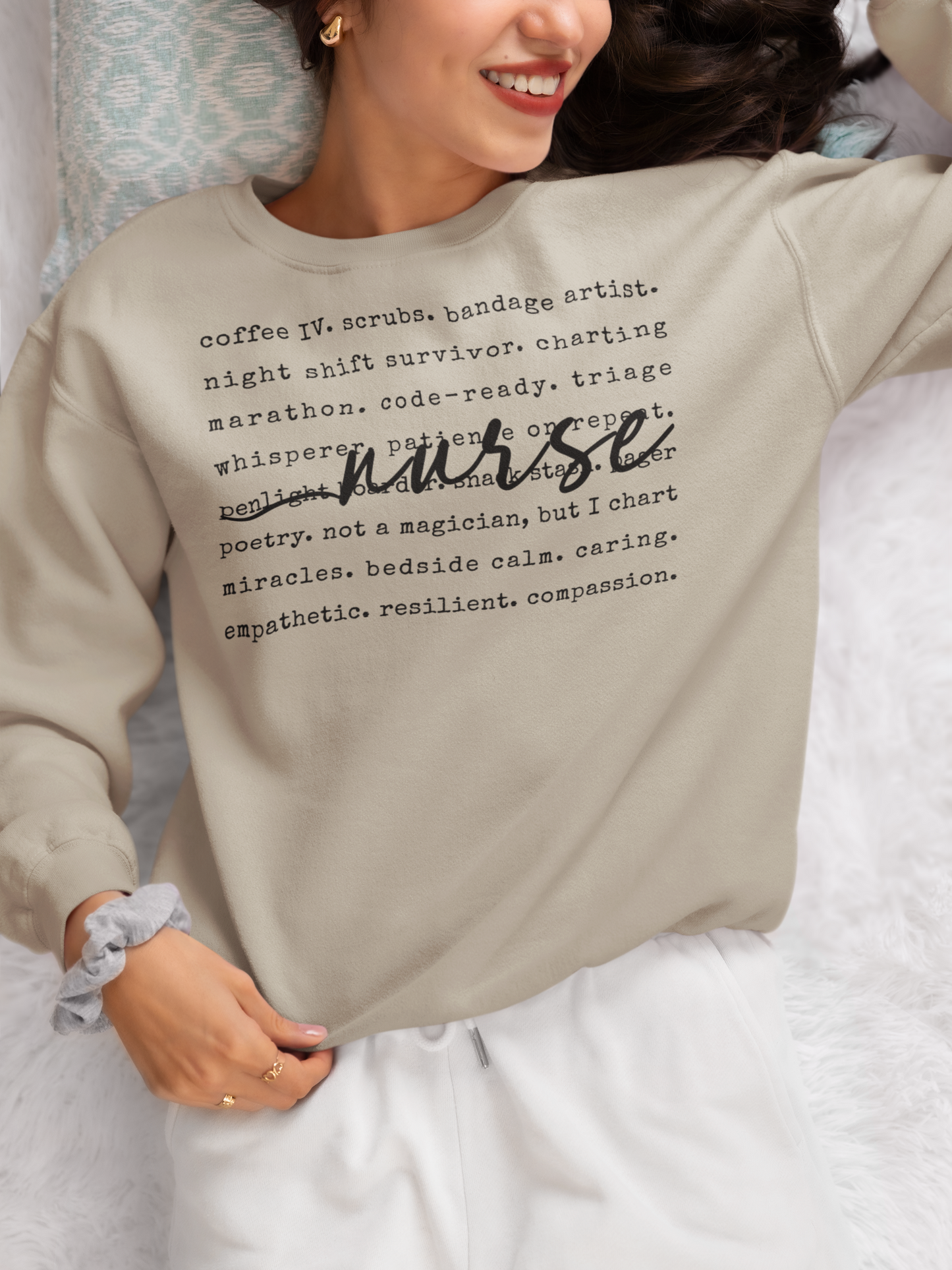 Person wearing a beige sweatshirt with text, sitting on a bed.