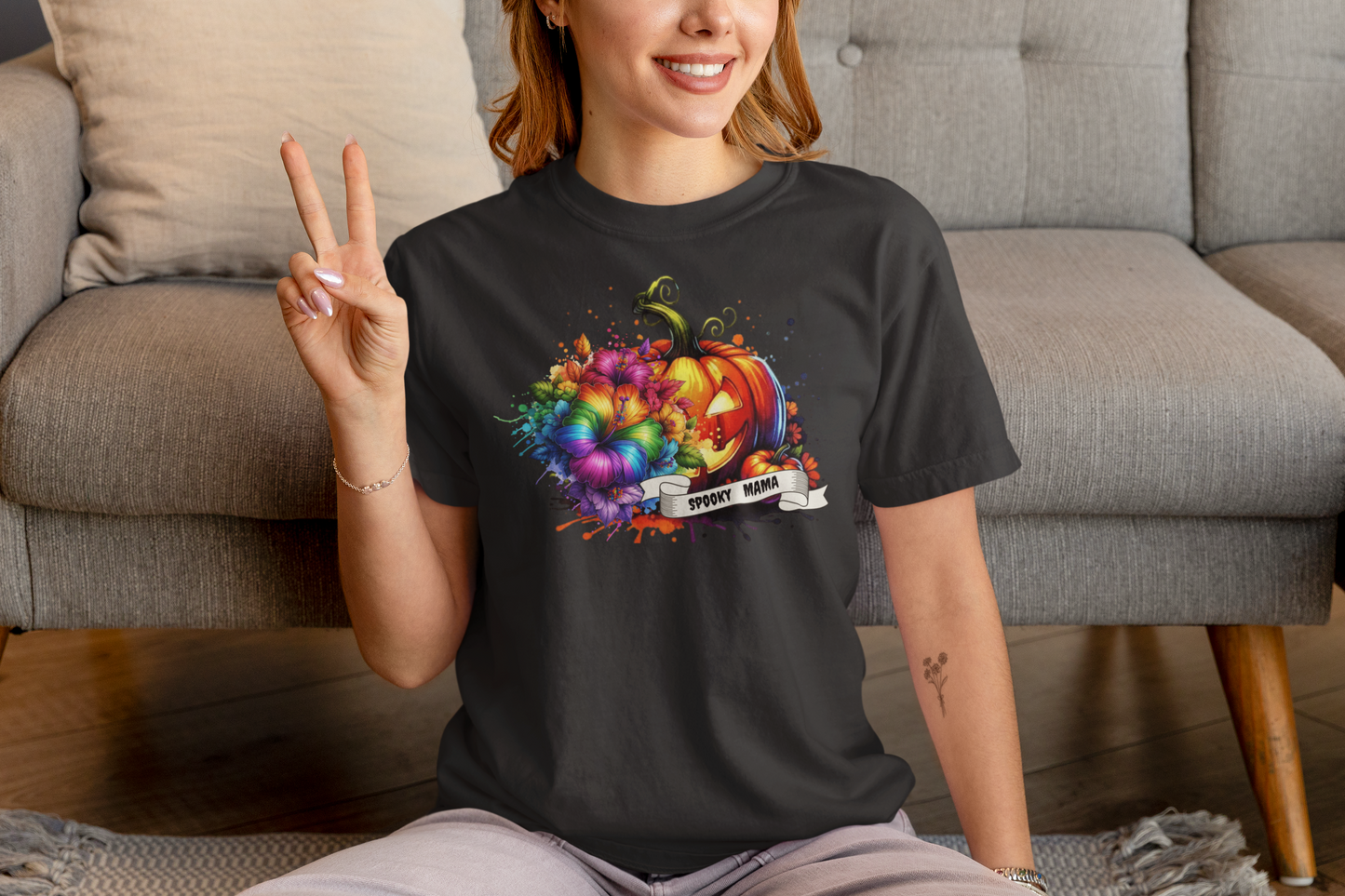 Person wearing a black t-shirt with a colorful pumpkin design, sitting on a couch.