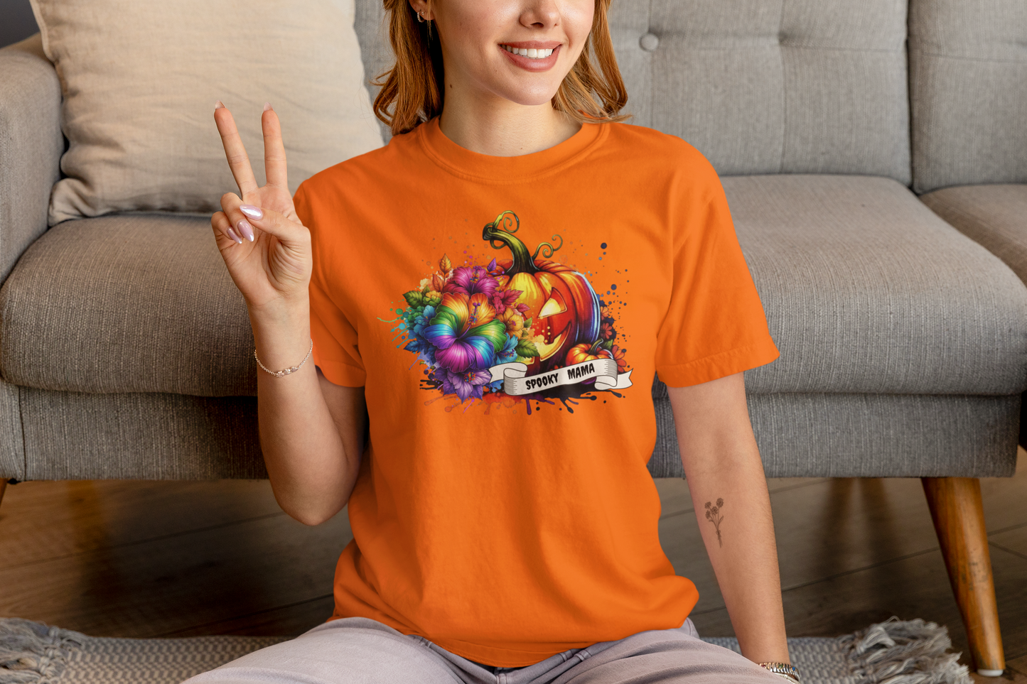 Person wearing an orange t-shirt with a colorful pumpkin design, sitting on a couch.