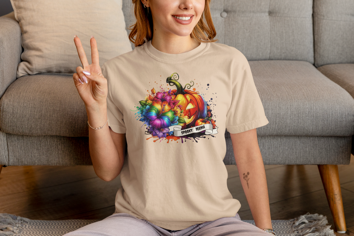 Person wearing a beige t-shirt with a colorful pumpkin design, sitting on a couch.