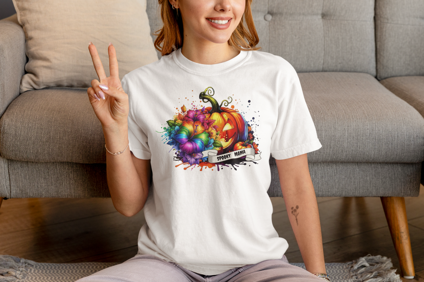 Person wearing a white t-shirt with a colorful pumpkin design, sitting on a couch.