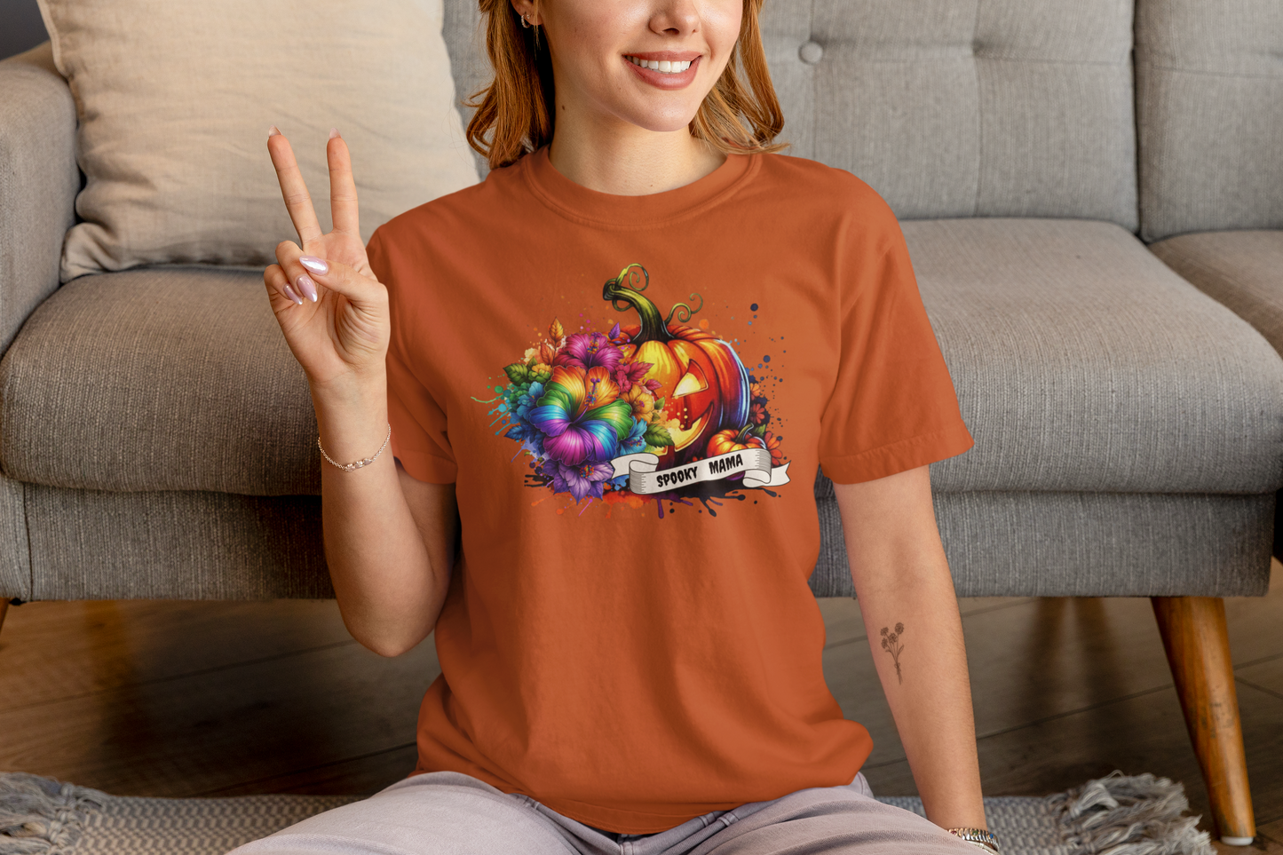 Person wearing an orange t-shirt with a colorful pumpkin design, sitting on a couch.
