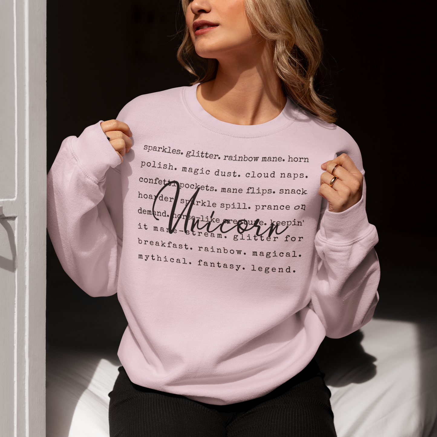 Person wearing a pink sweatshirt with text design, sitting on a white surface.