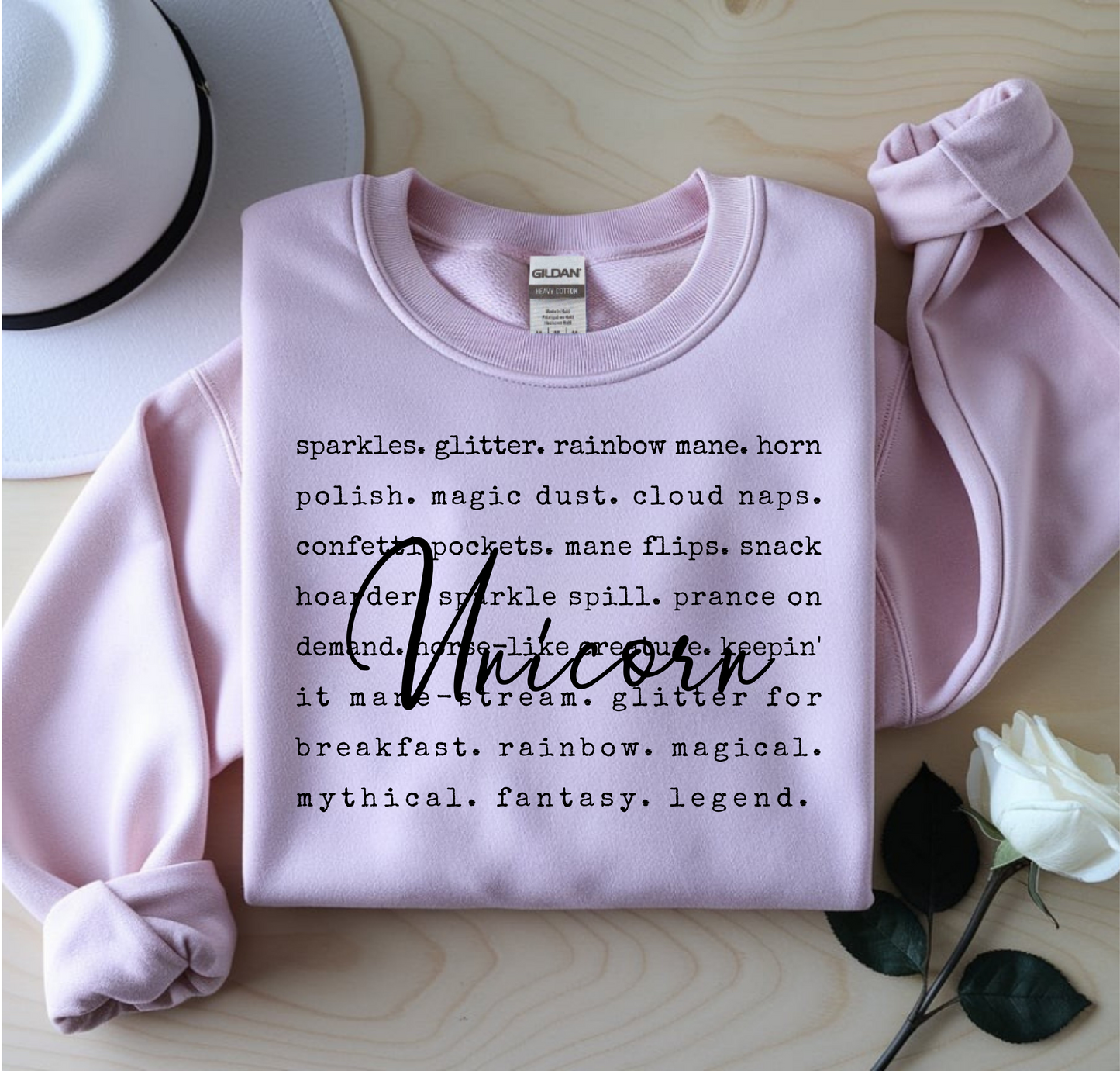 Pink sweatshirt with text on a wooden surface with a white rose.