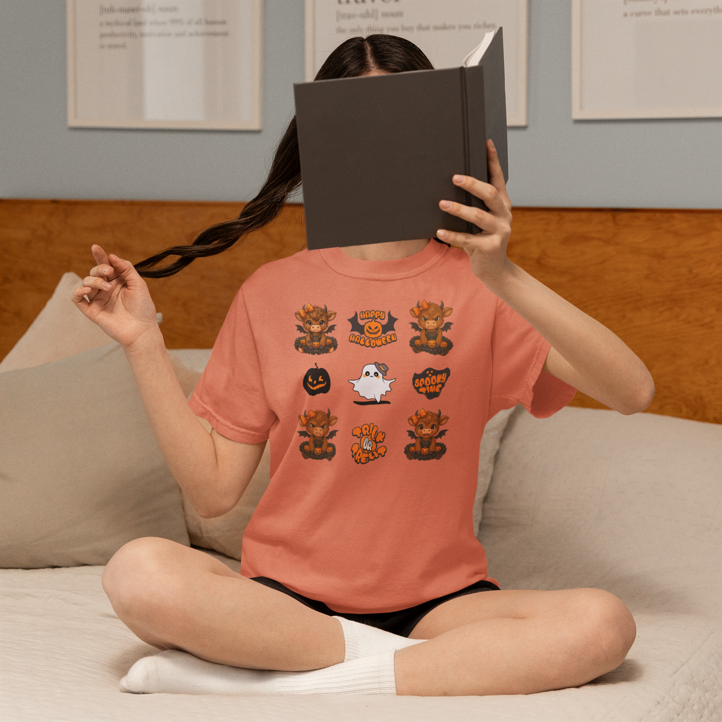 Person wearing a Halloween-themed t-shirt sitting on a couch with a book covering their face.