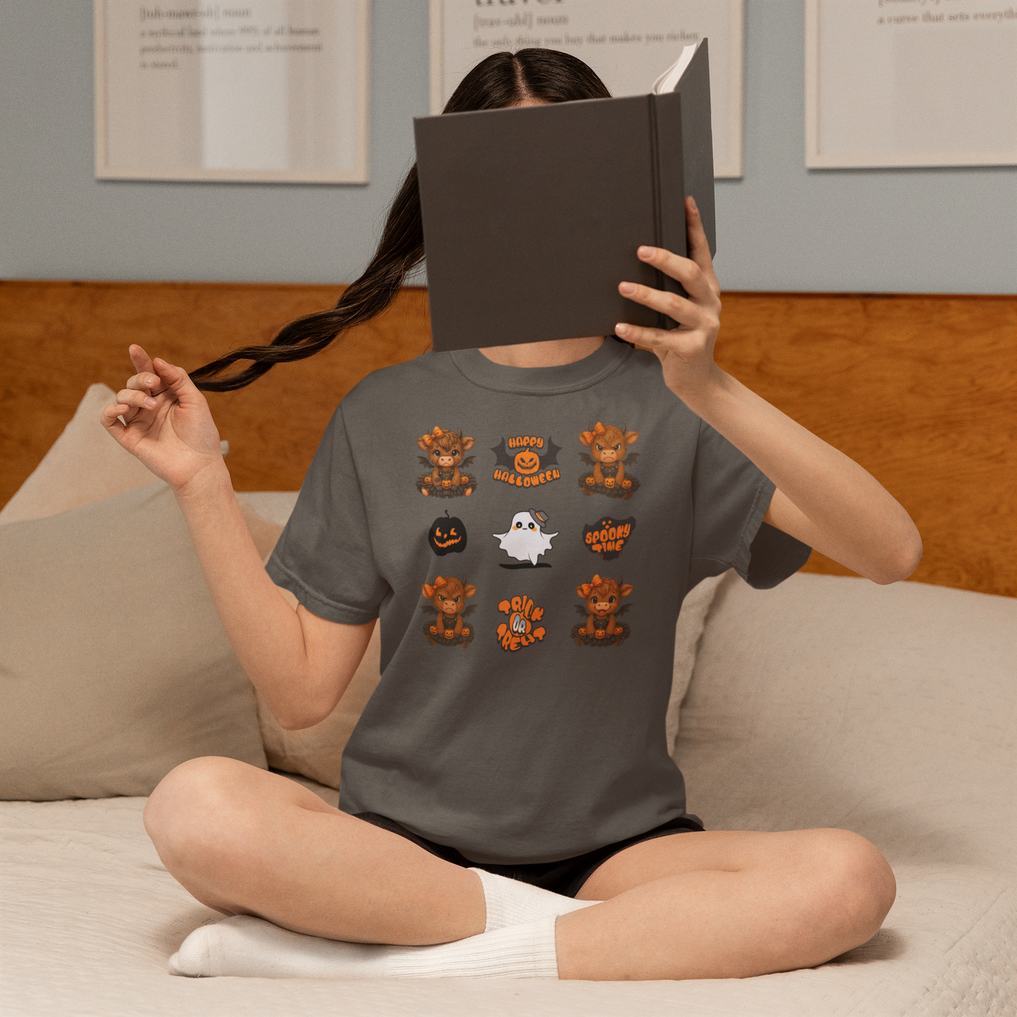 Person wearing a Halloween-themed t-shirt sitting on a couch with a book covering their face.