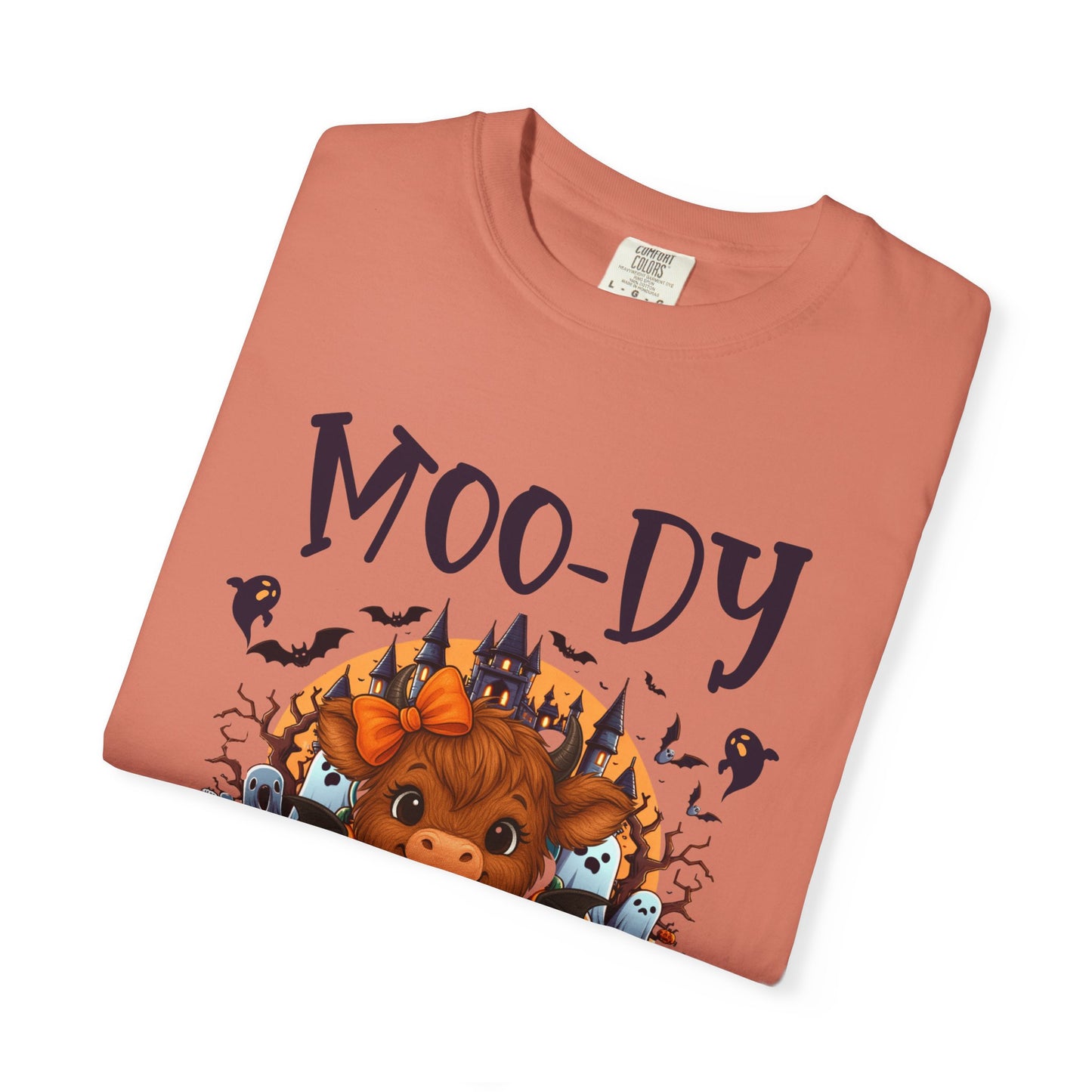 Folded terracotta-colored t-shirt with 'MOODY' design featuring a cow, castle, and bats on a white background.