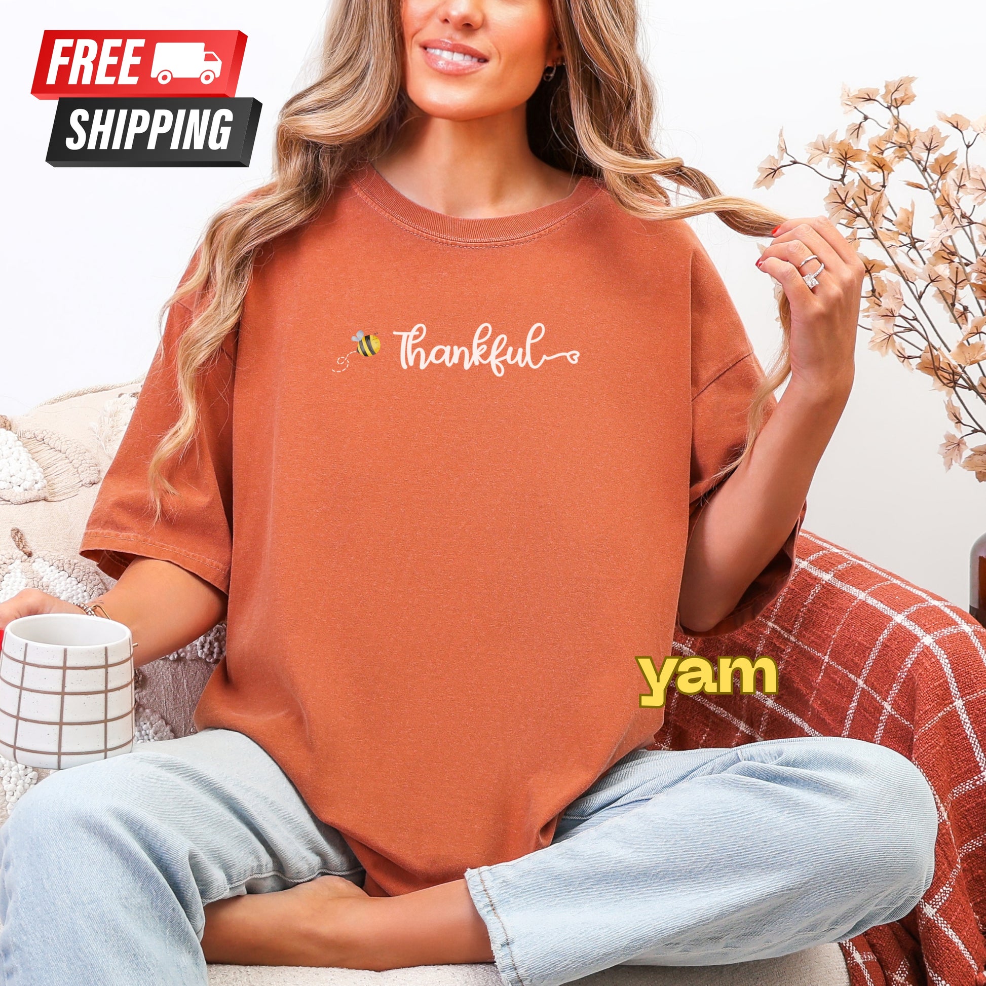 Person wearing a 'Thankful' t-shirt with 'yam' text, sitting on a couch with free shipping label.
