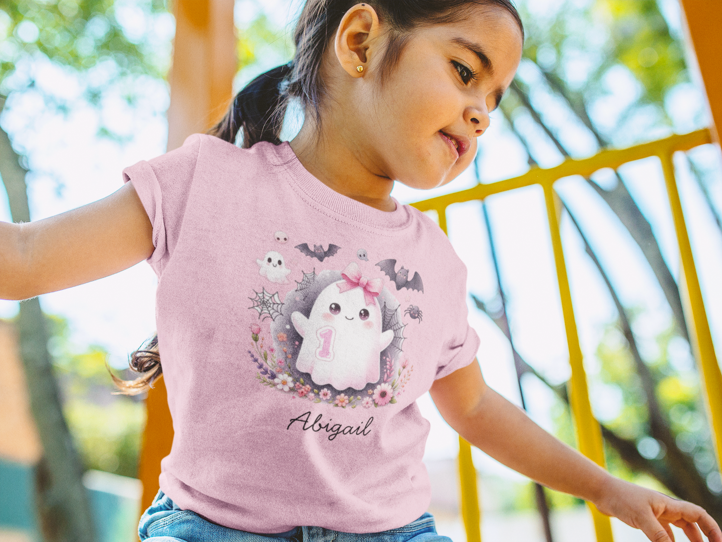 Child wearing a pink t-shirt with a cartoon character and 'Abigail' text, sitting outdoors.