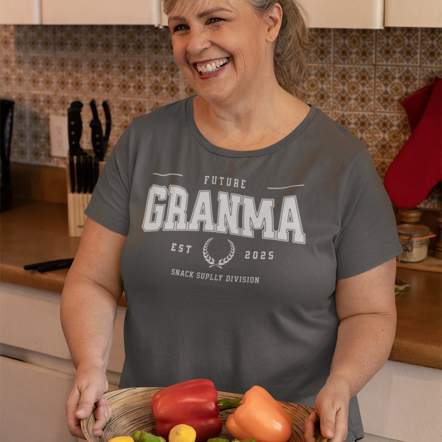 Woman wearing a 'Future Grandma' t-shirt in a kitchen holding a basket of vegetables.