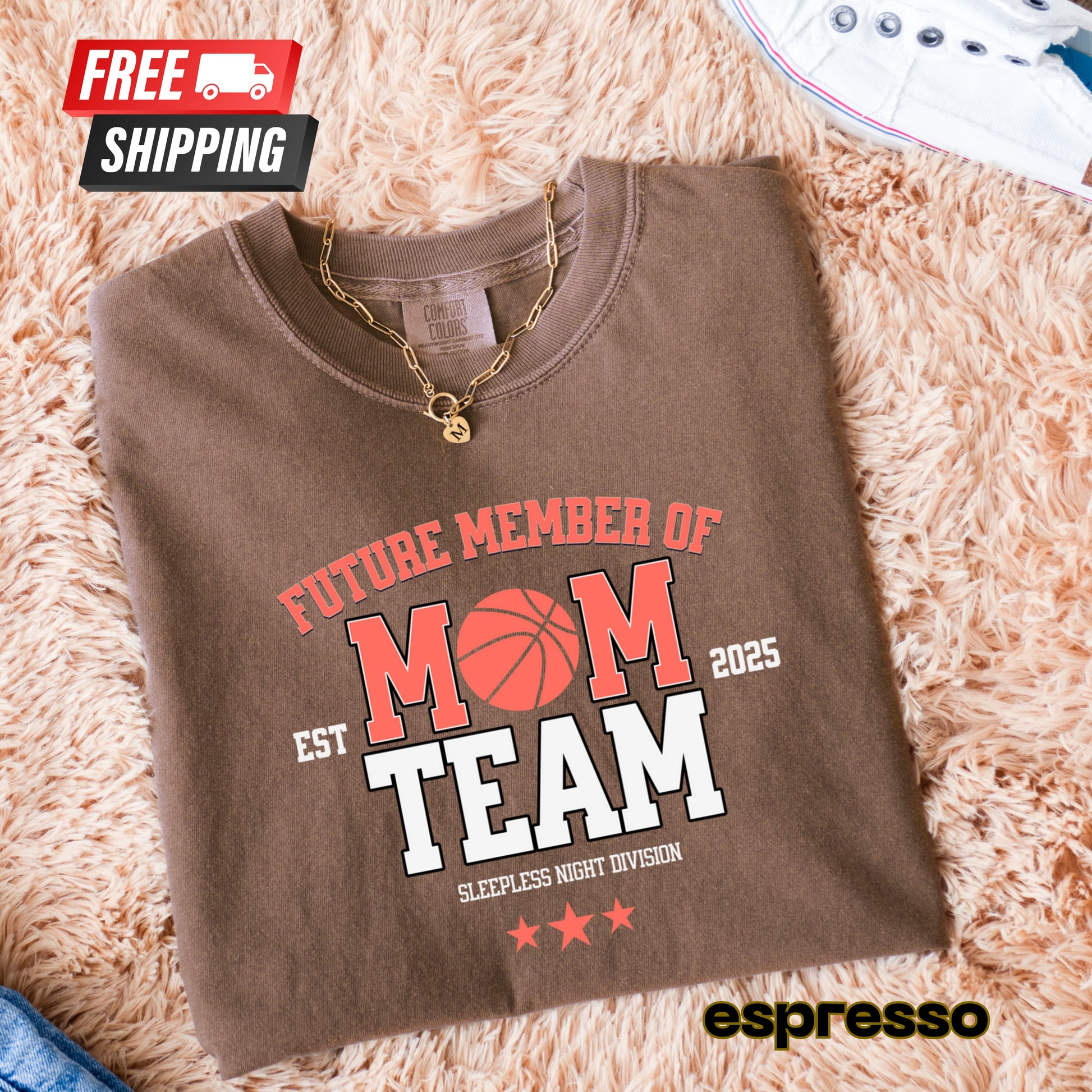 Folded brown sweatshirt with 'Future Member of Mom Team' text on a fluffy beige surface, featuring free shipping icon.