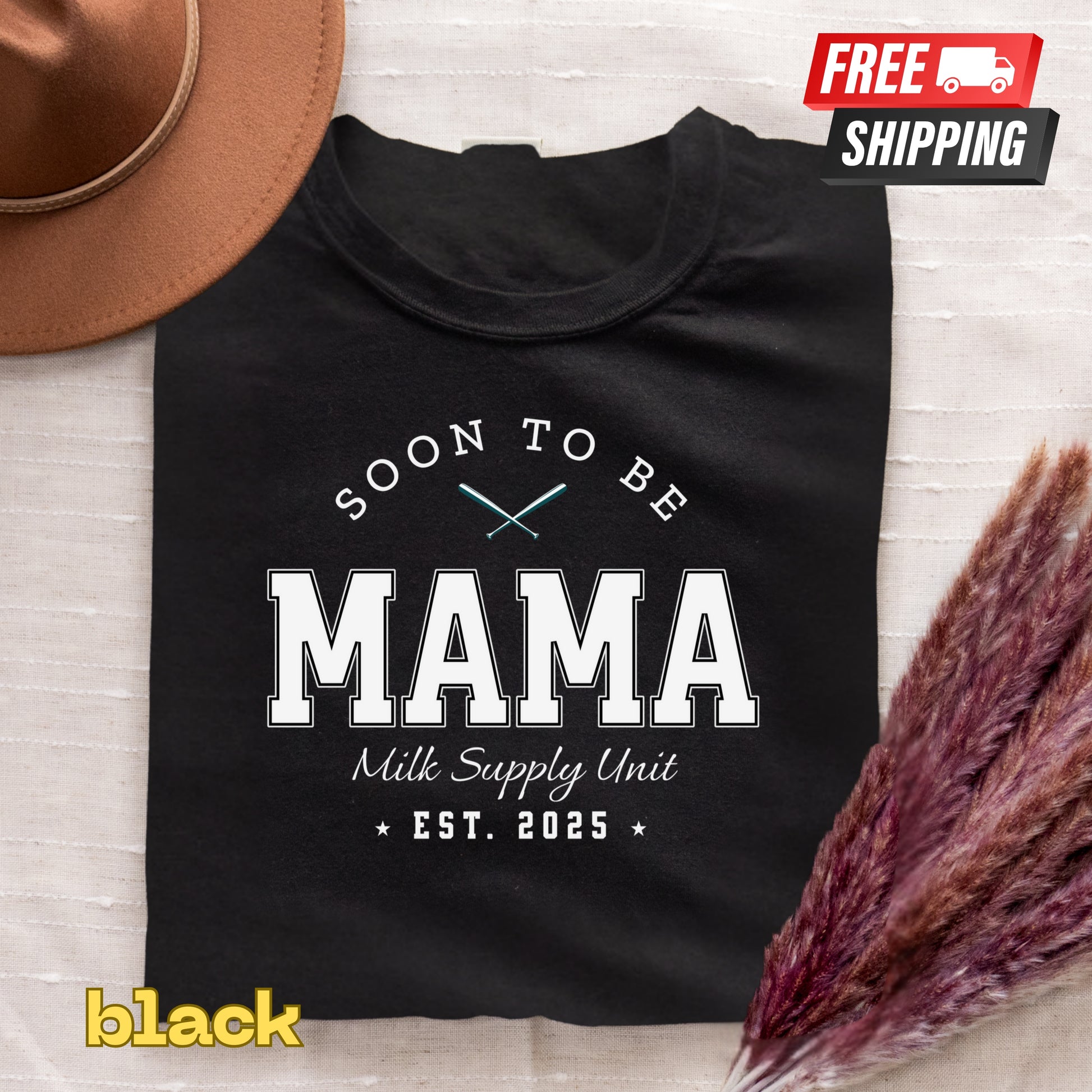 Black t-shirt with 'Soon to be Mama' text on a textured surface with a hat and dried flowers.