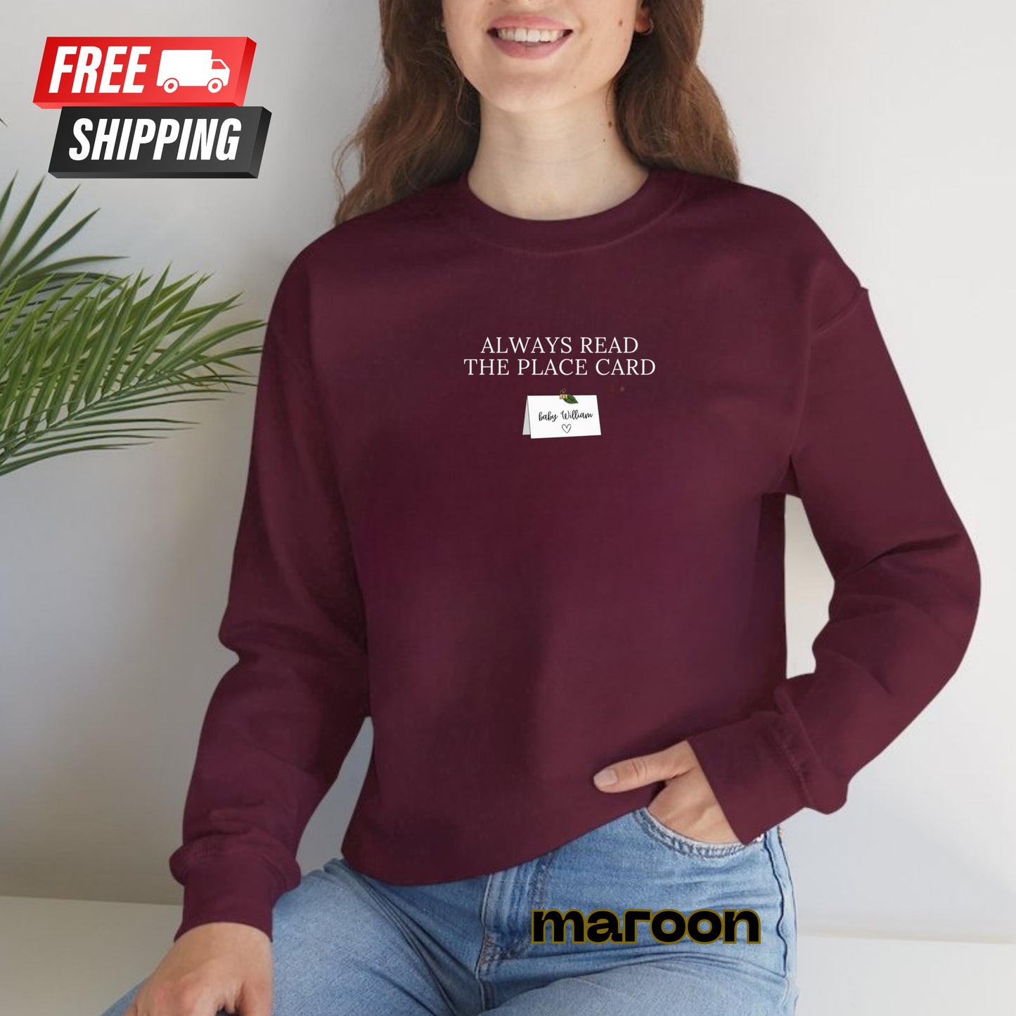 Person wearing a maroon sweatshirt with text and a small card, sitting against a light background.
