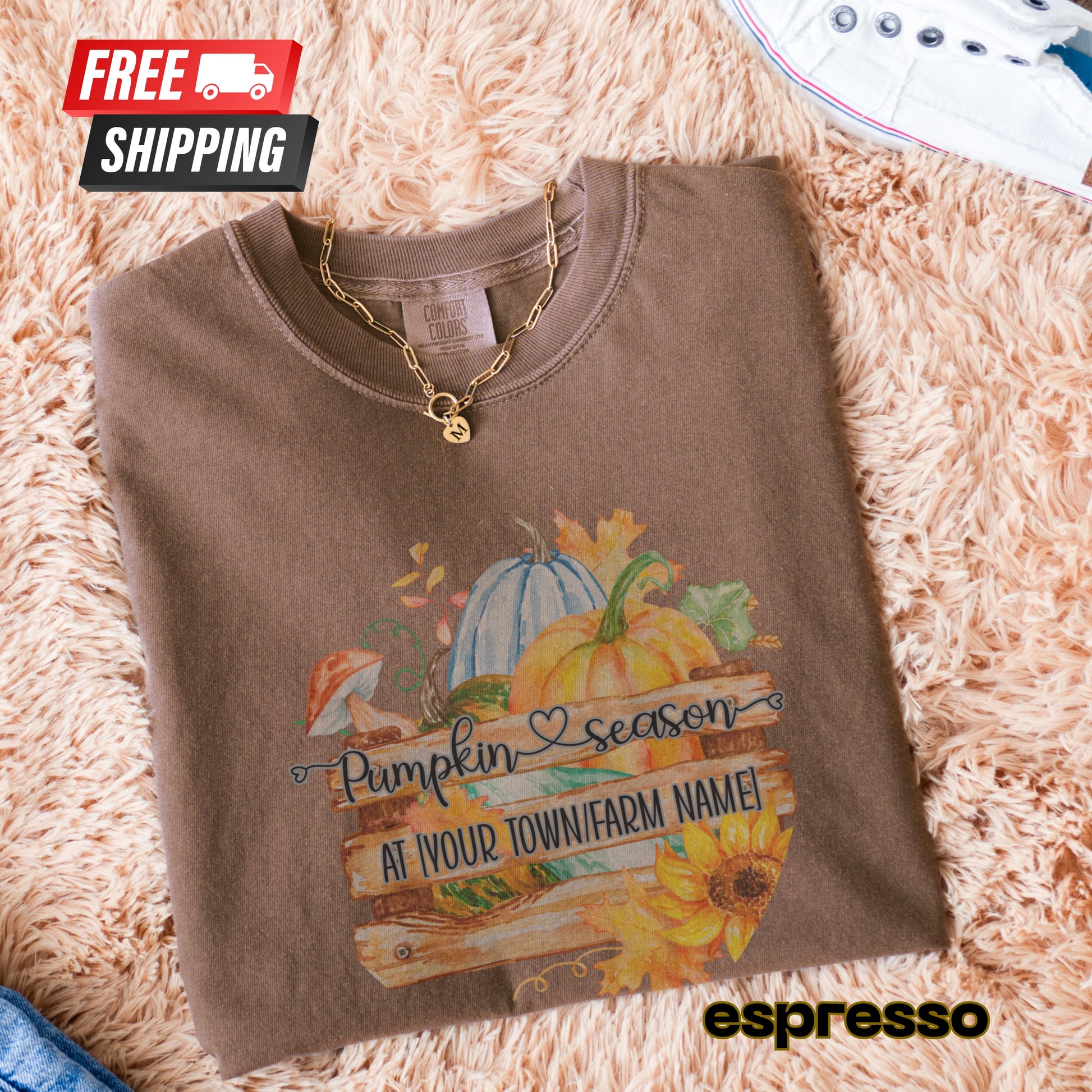 Folded brown sweatshirt with pumpkin season design on a fluffy beige surface, featuring free shipping text.