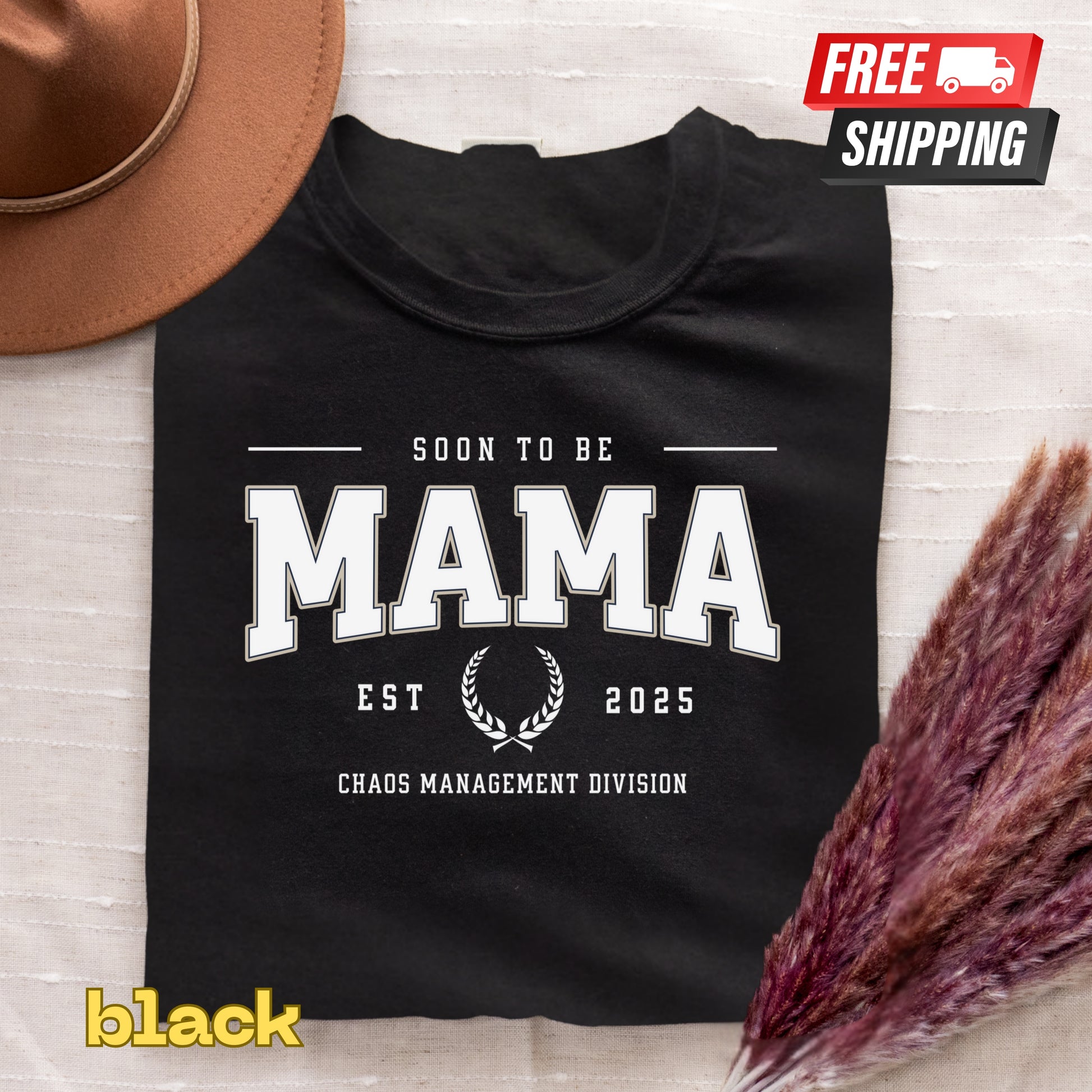 Black t-shirt with 'Soon to be Mama' text on a textured surface with a hat and dried flowers.