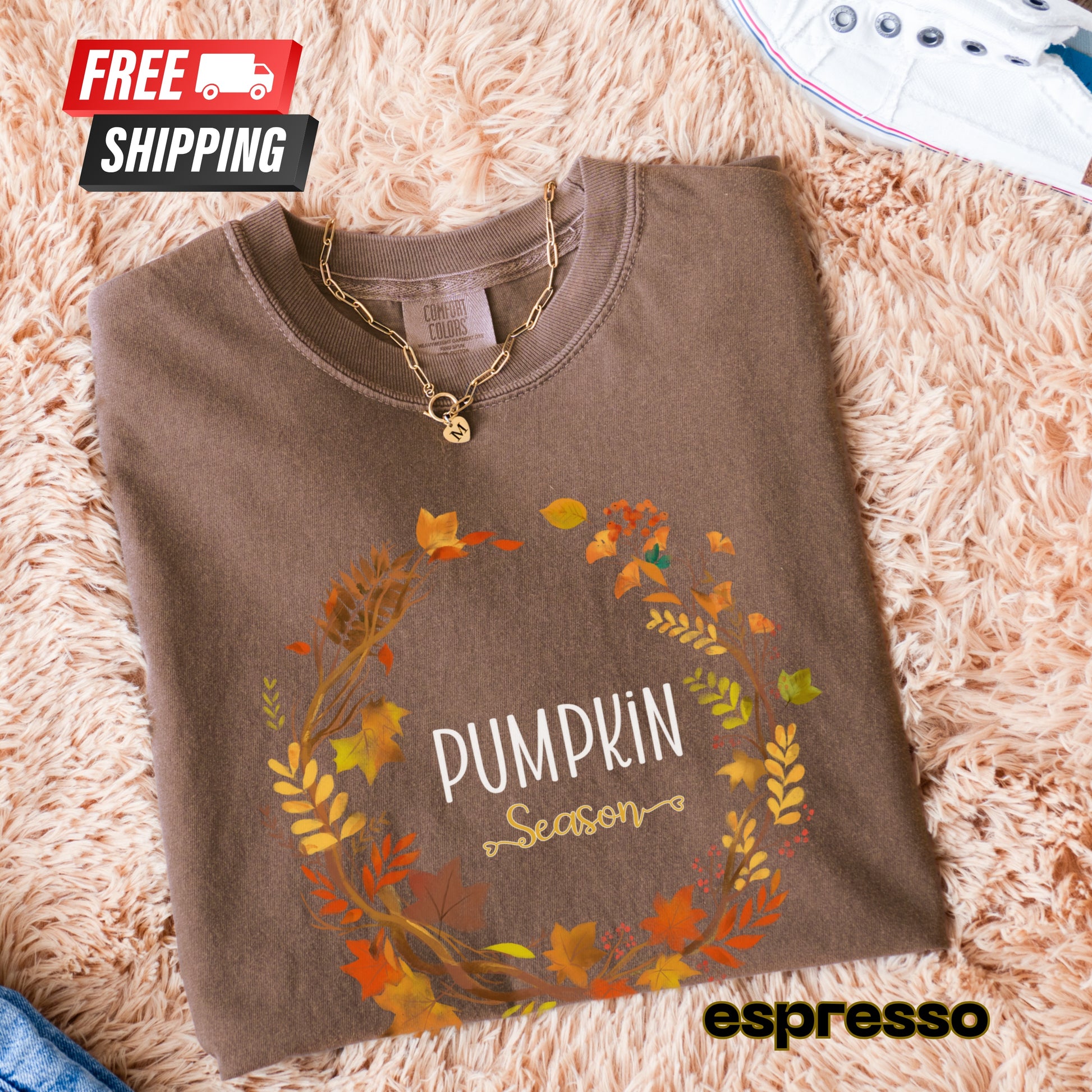 Folded brown sweatshirt with 'Pumpkin Season' design on a fluffy beige surface, featuring free shipping icon and espresso brand name.