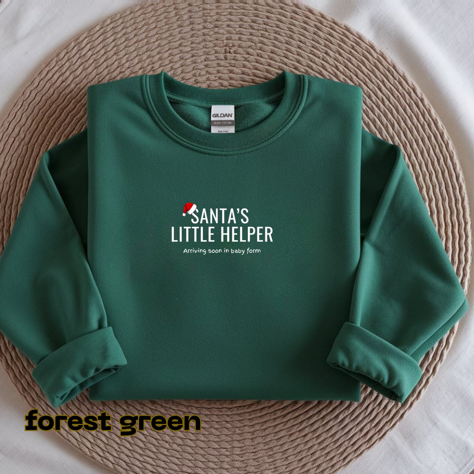 Green sweatshirt with 'Santa's Little Helper' text on a woven mat