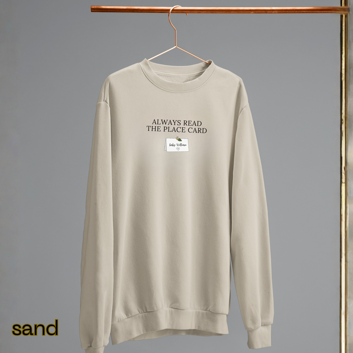 Beige sweatshirt with text on a hanger against a gray background