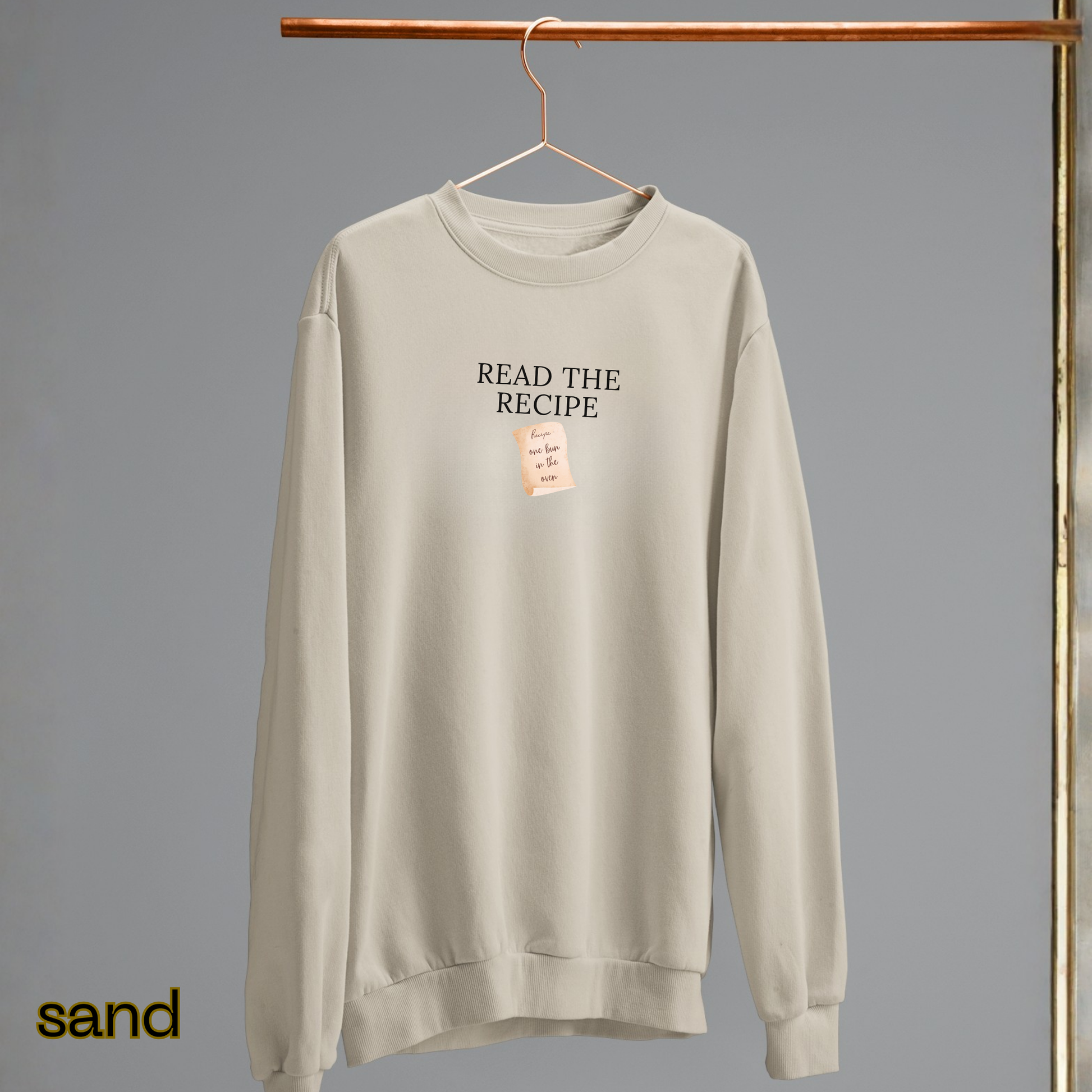 Beige sweatshirt with 'READ THE RECIPE' text on a hanger against a gray background