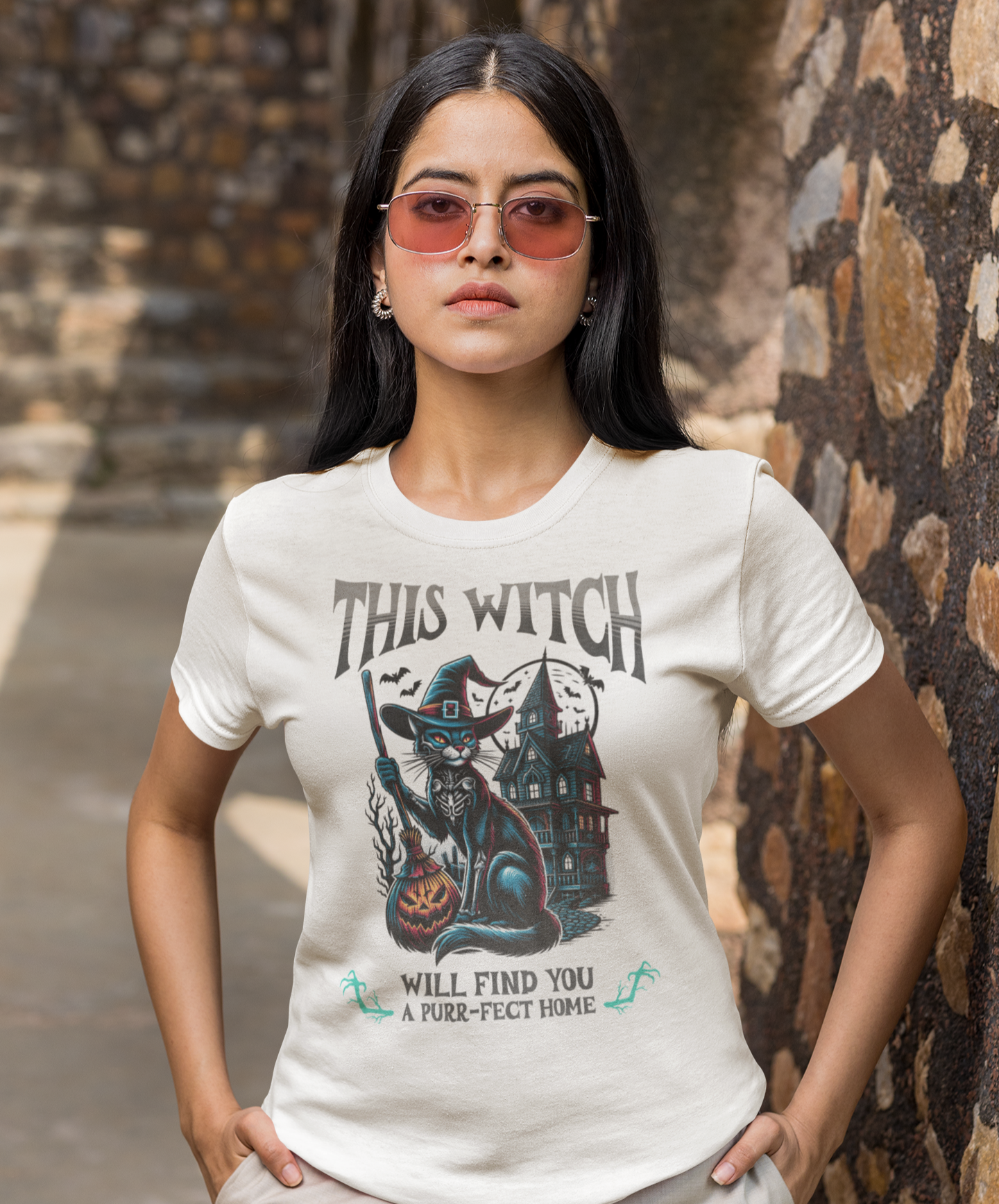 Woman wearing a white t-shirt with a graphic design and text, standing against a stone wall.