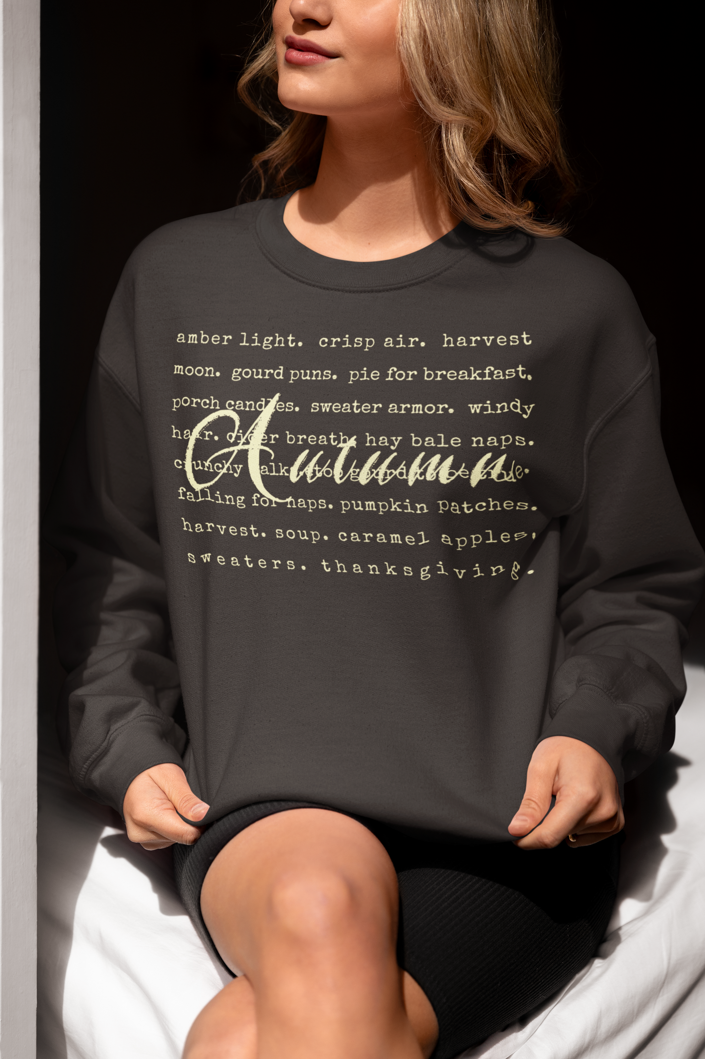 Person wearing a dark gray sweatshirt with 'Autumn' text, sitting on a white surface.