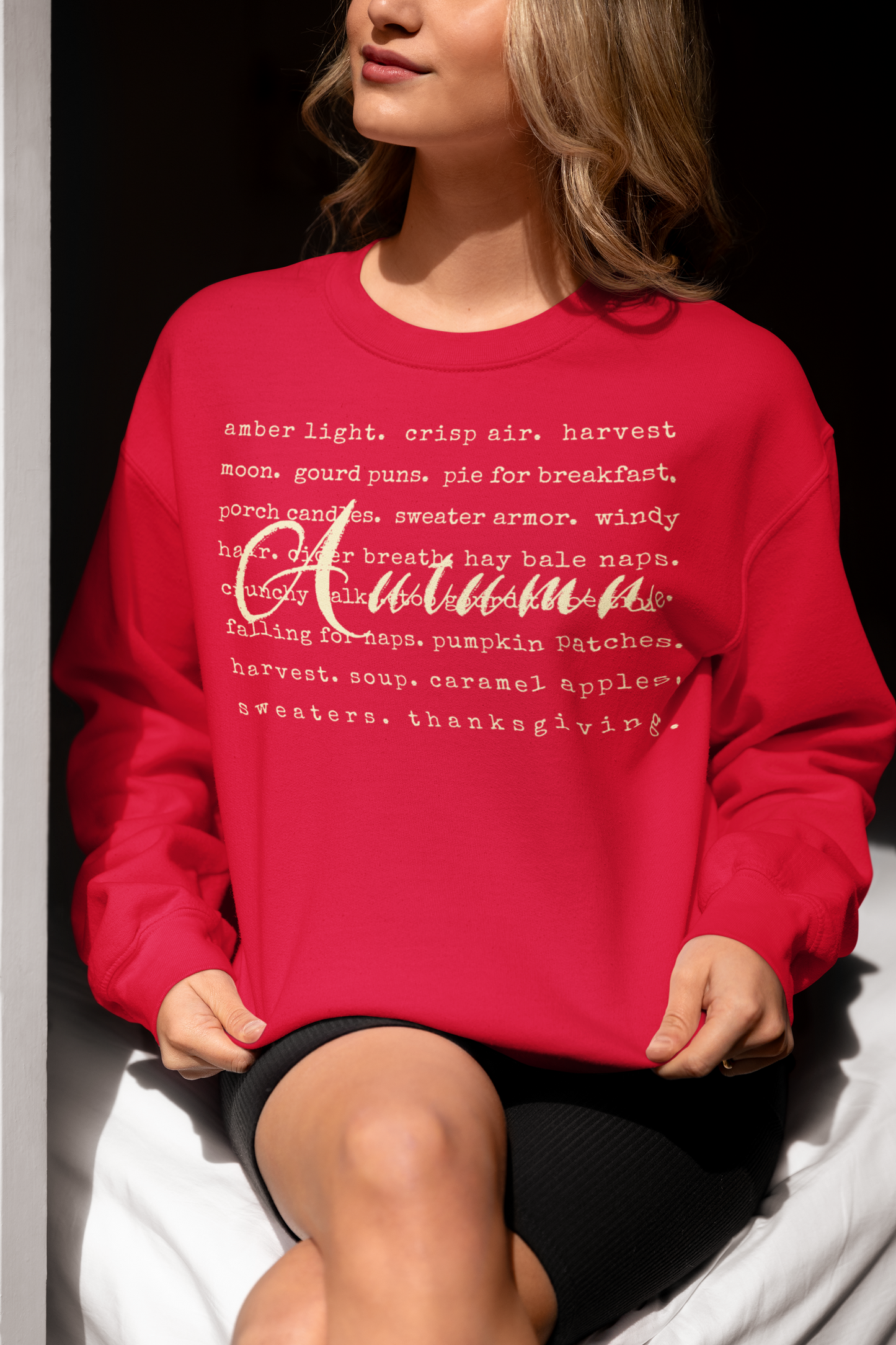 Person wearing a red sweatshirt with white text sitting on a white surface.